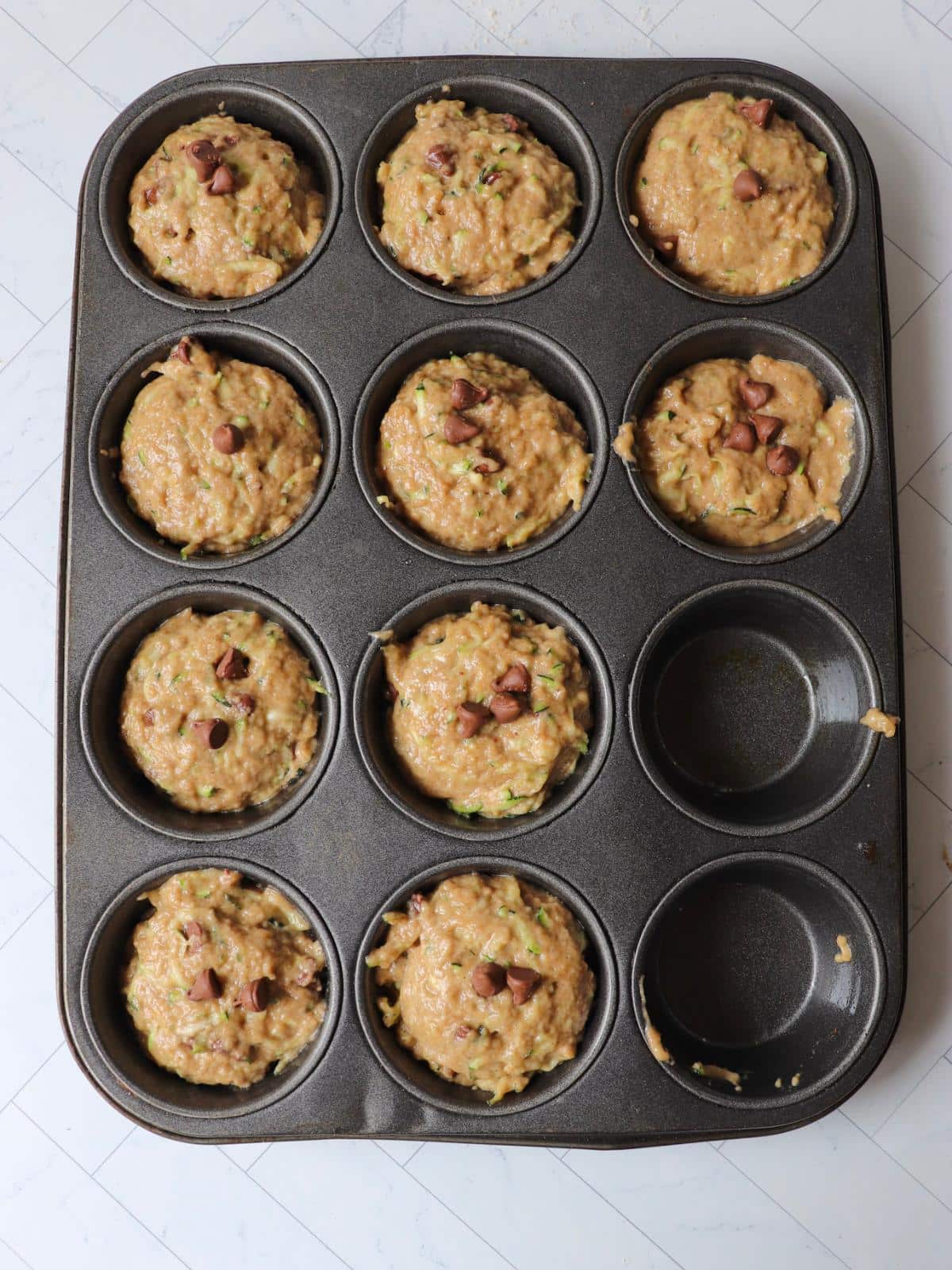Vegan zucchini muffins in a muffin tin before getting baked.