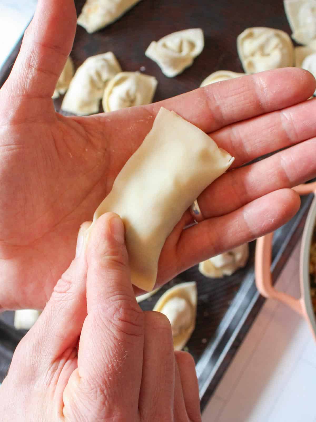 Hand folding over a square dumpling.