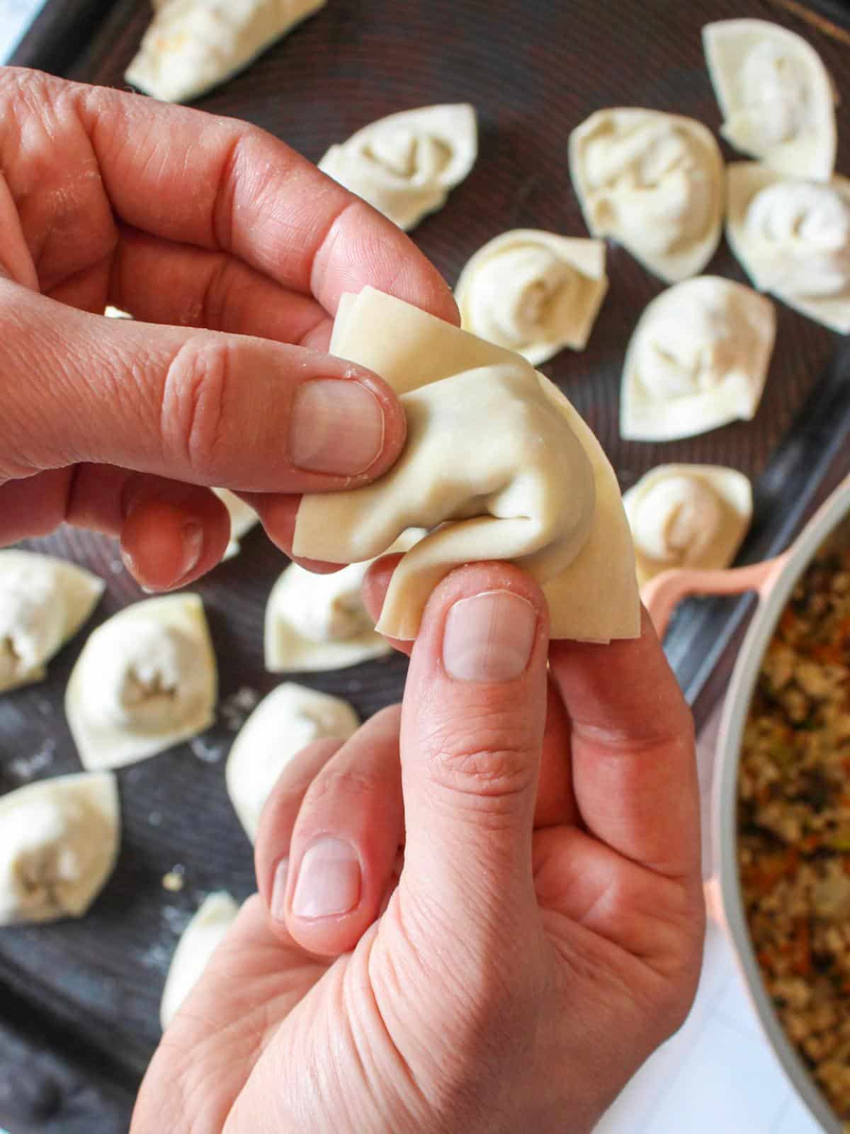 Hand folding a square vegan dumpling.