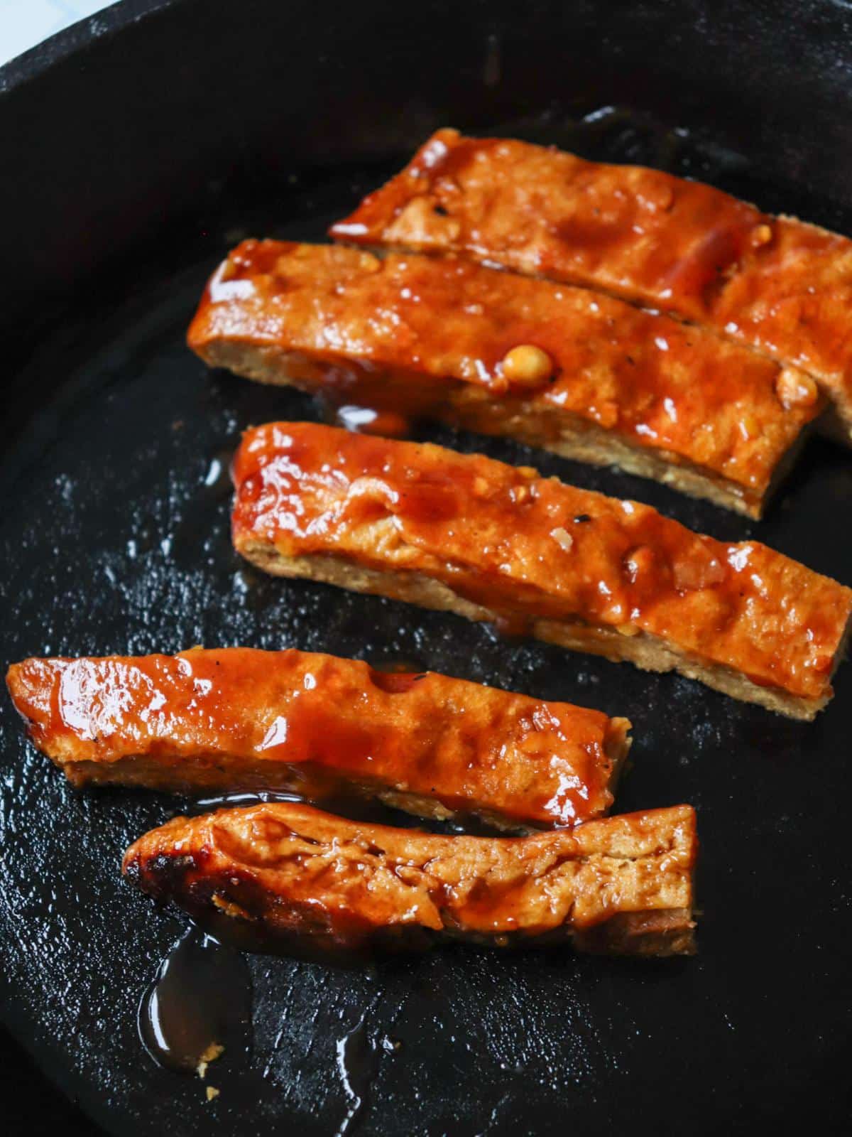 Vegan ribs grilling in a grill pan with bbq sauce.