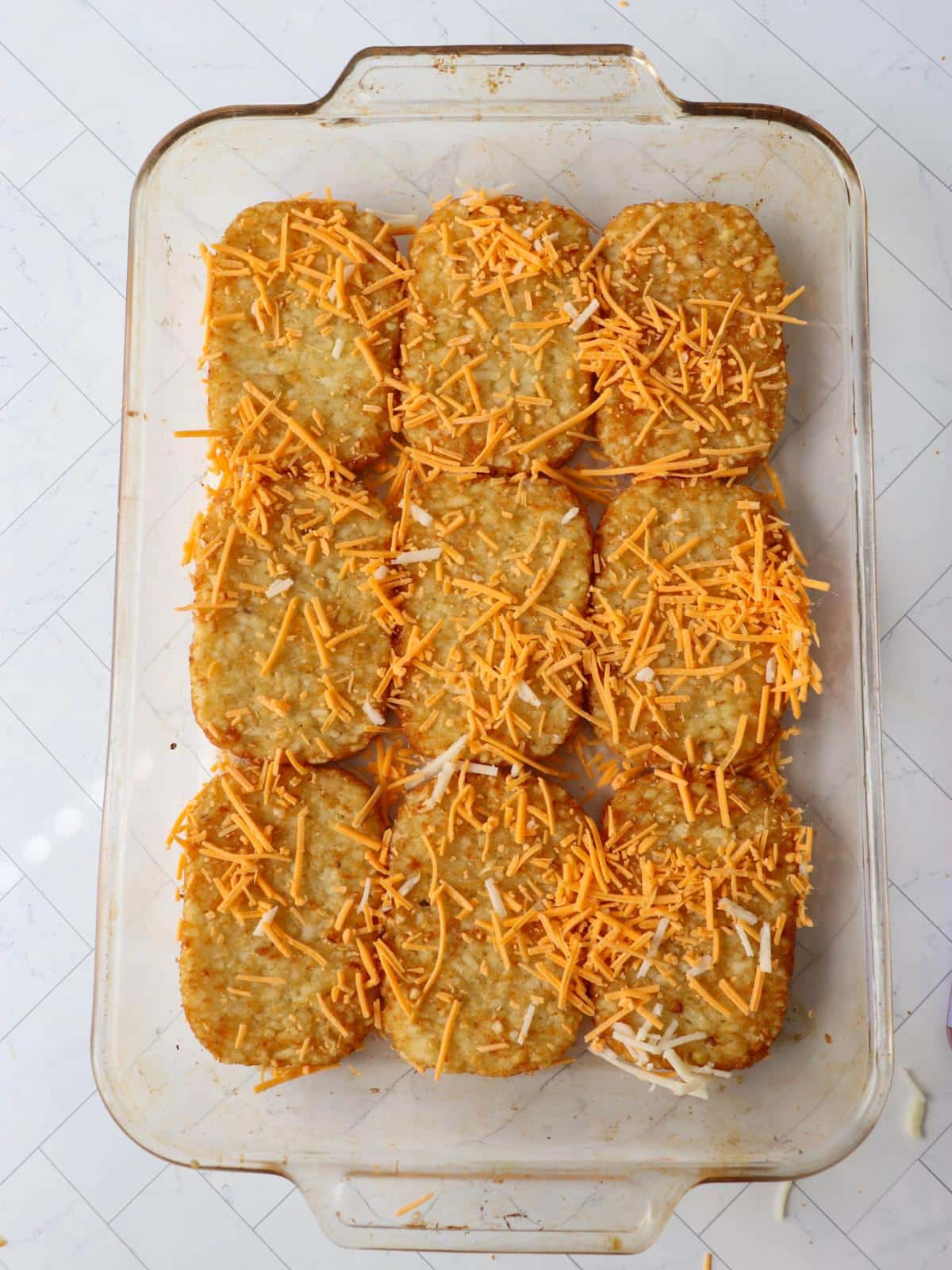 Hash brown patties and vegan cheese in a casserole dish.