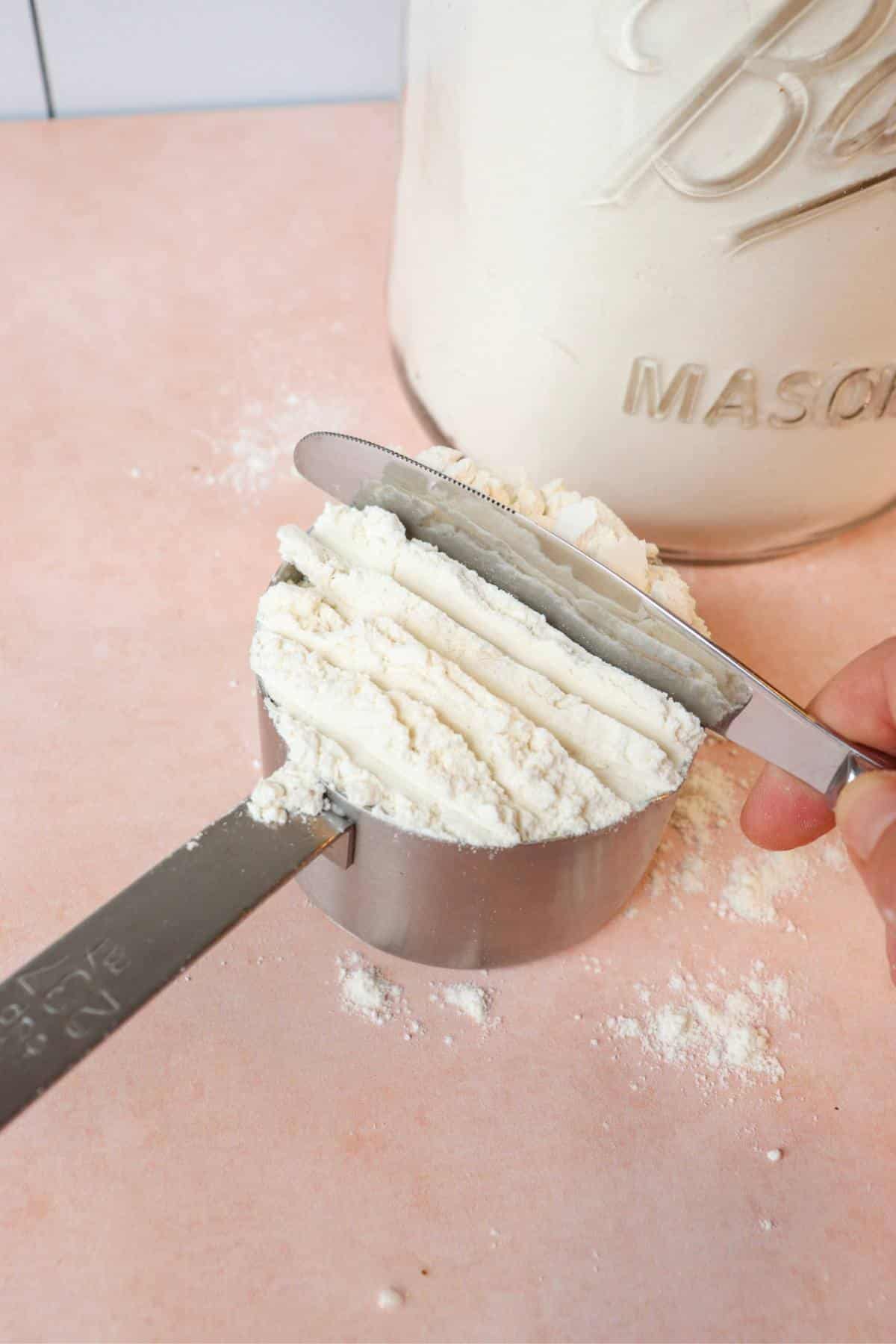 Bread flour being measured out in a measuring cup.