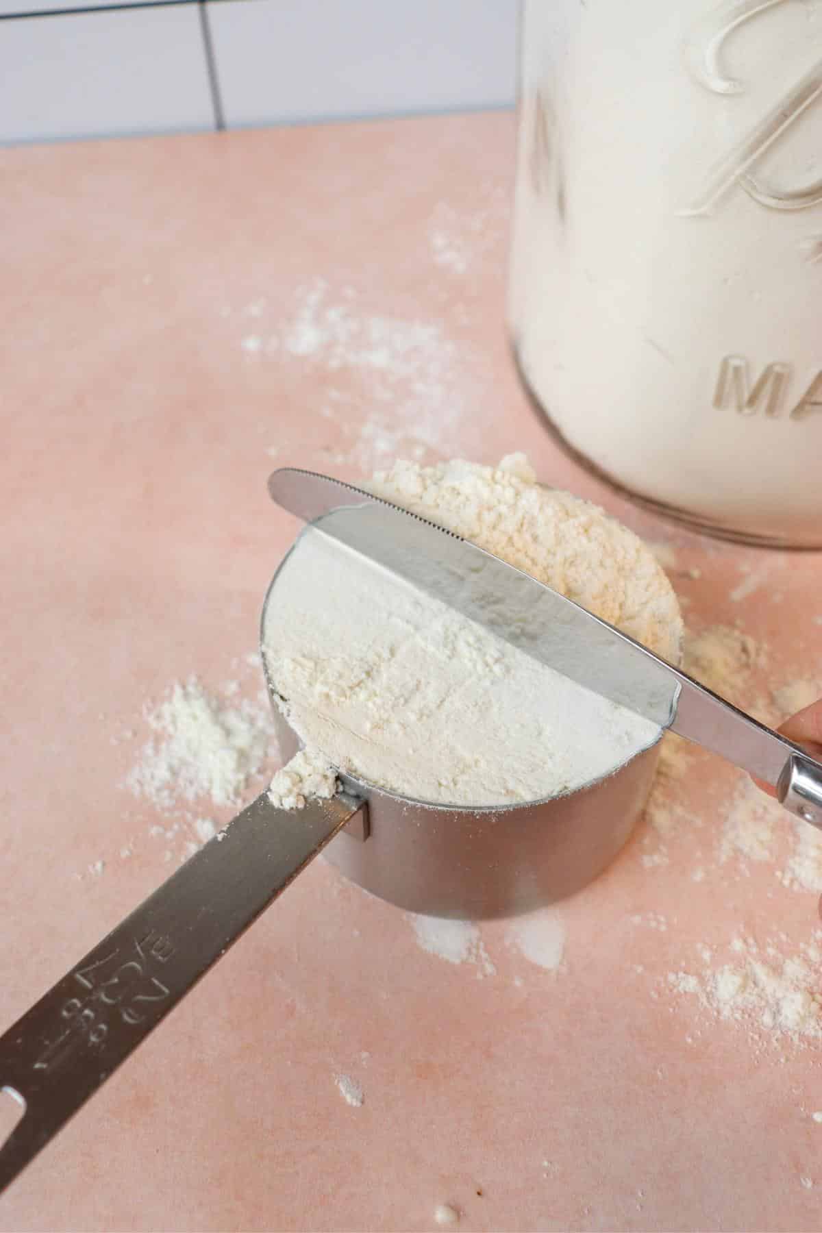 Flour in a measuring cup getting leveled off by the back of a butter knife.
