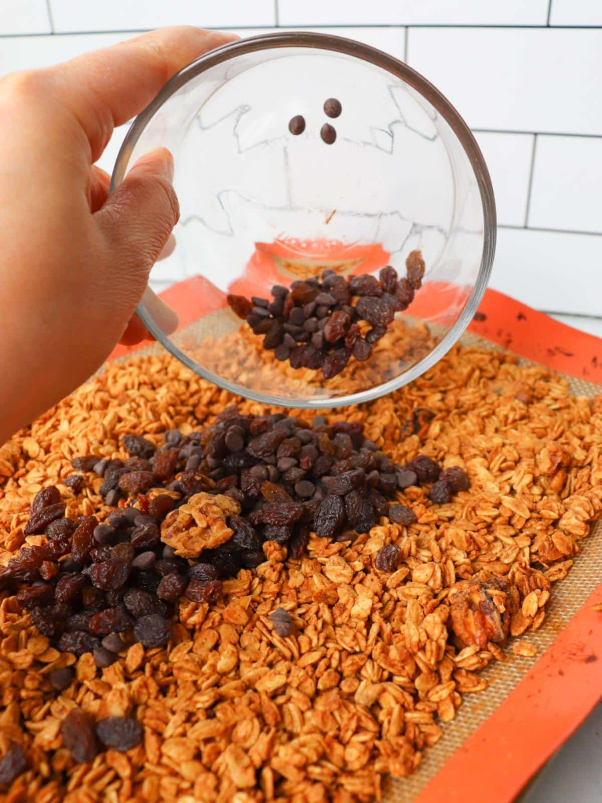A hand mixing in raisins and chocolate chips into vegan granola.
