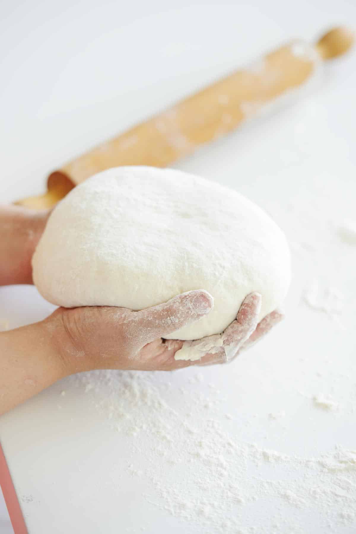 Hand rolling bread dough into an oval shape on a floured surface