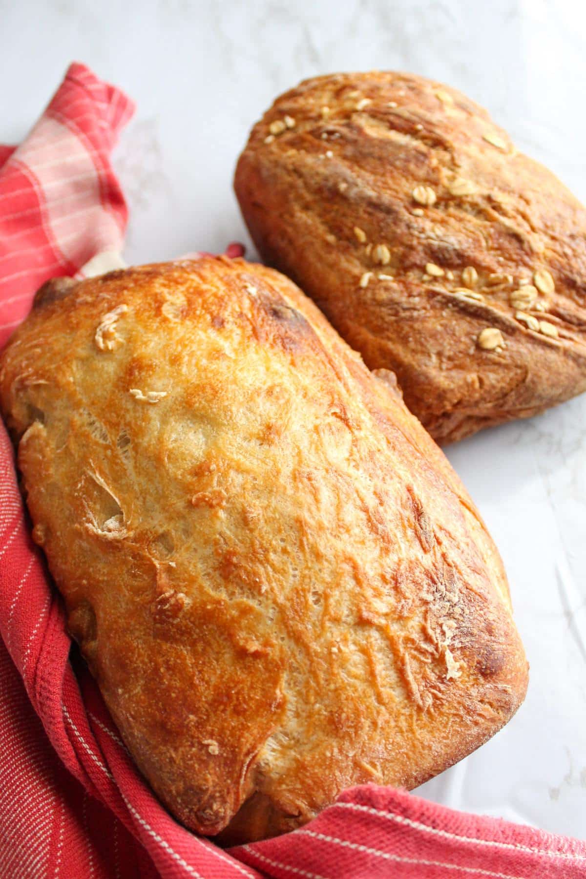 Two loaves of vegan bread on a counter next to a red kitchen towel. 