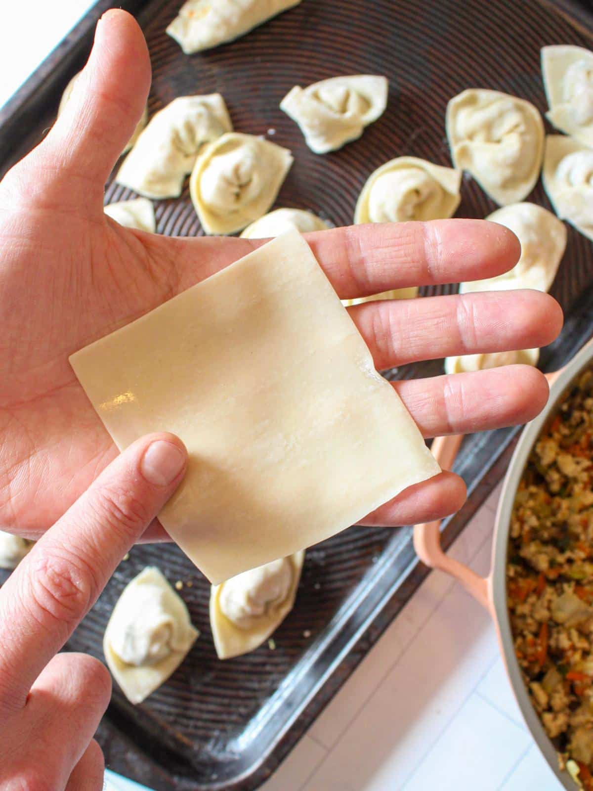 Hand holding a square dumpling wrapper, wetting the edges.