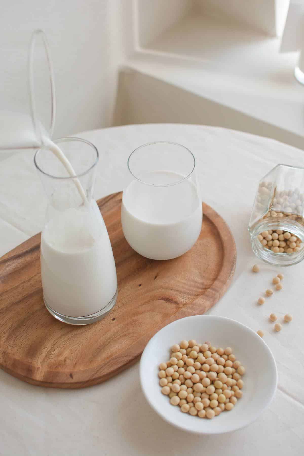 Soy milk being poured into a glass with a bowl of soy beans next to it.