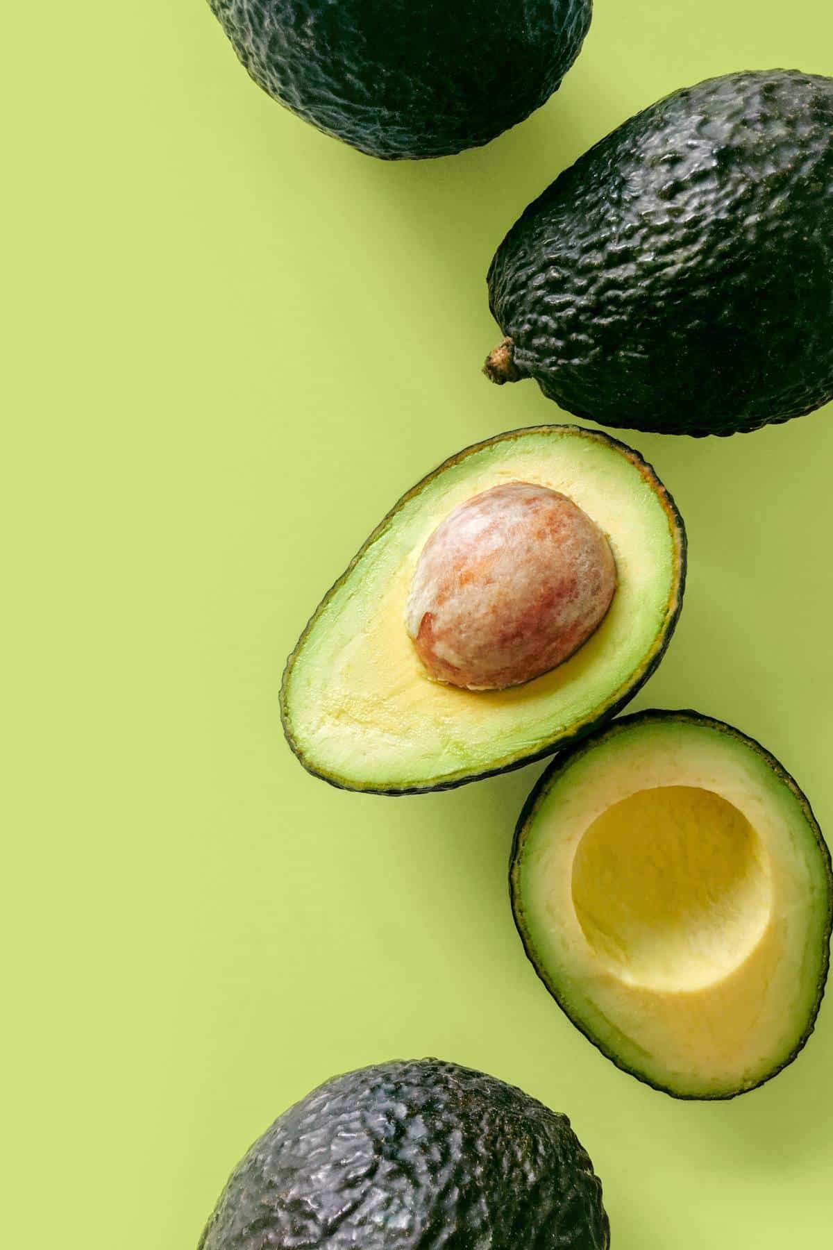 Four avocados on a table with one of them cut open.