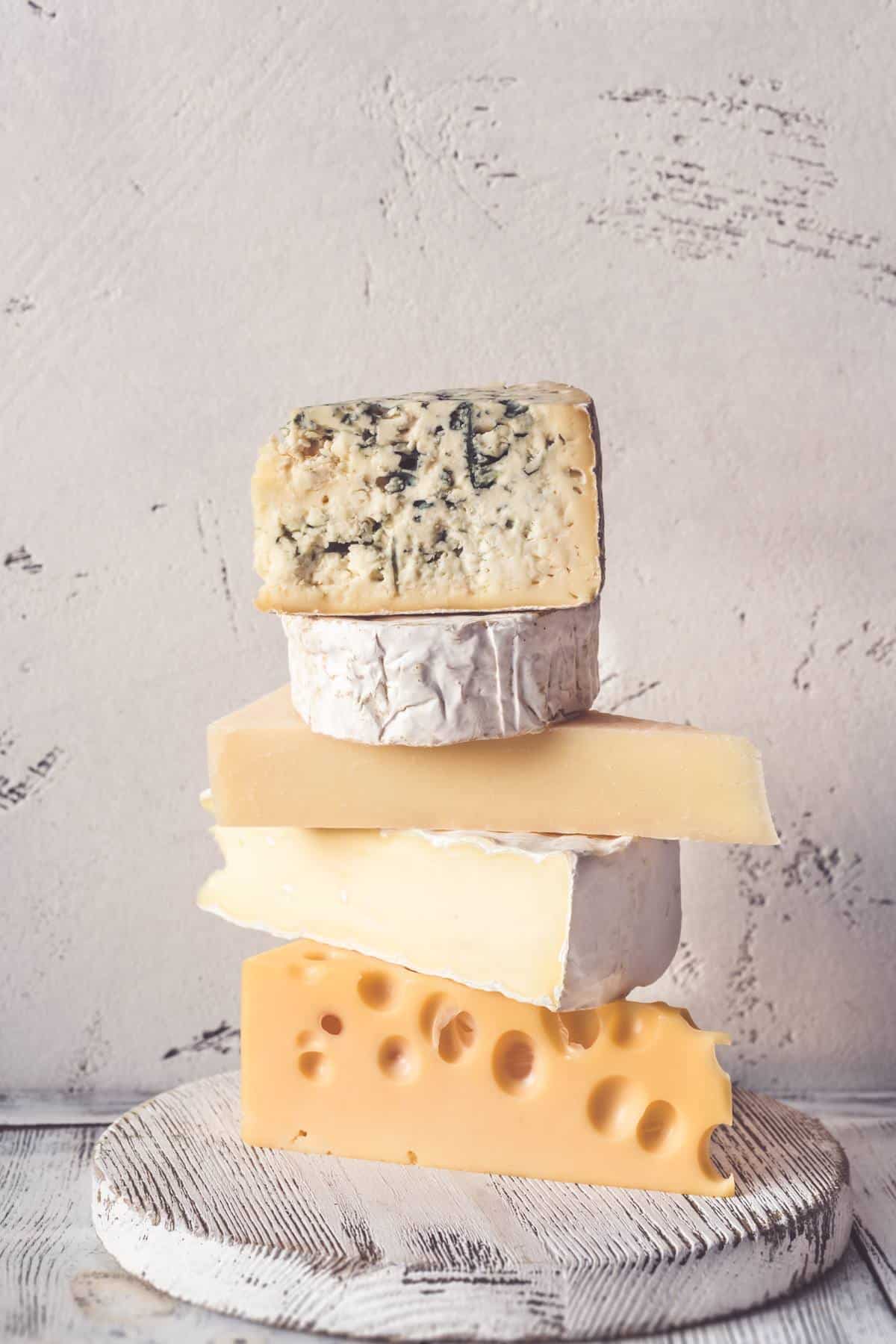 Five different types of cheese stacked on top of each other on a wooden cutting board.