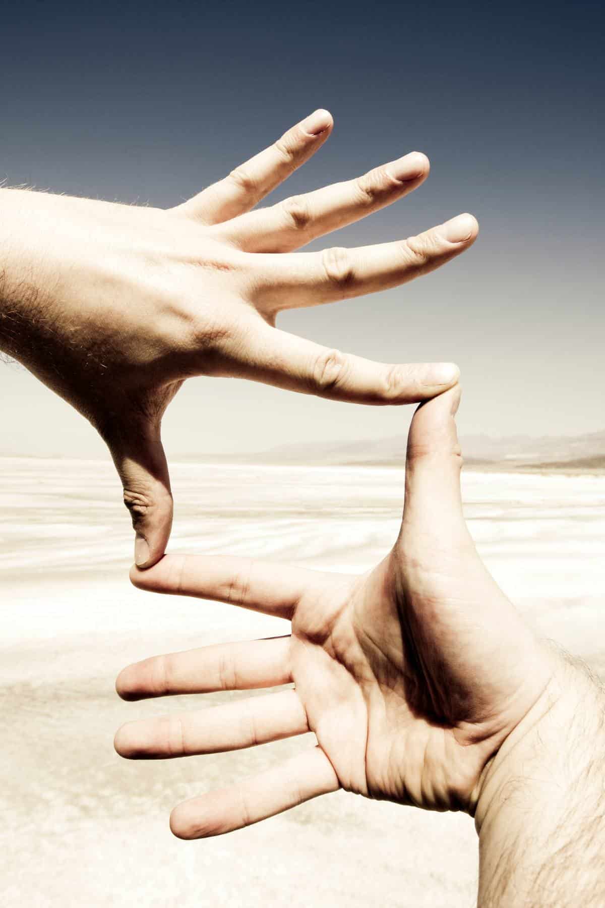 A hand making she shape of a frame with a desert in the background