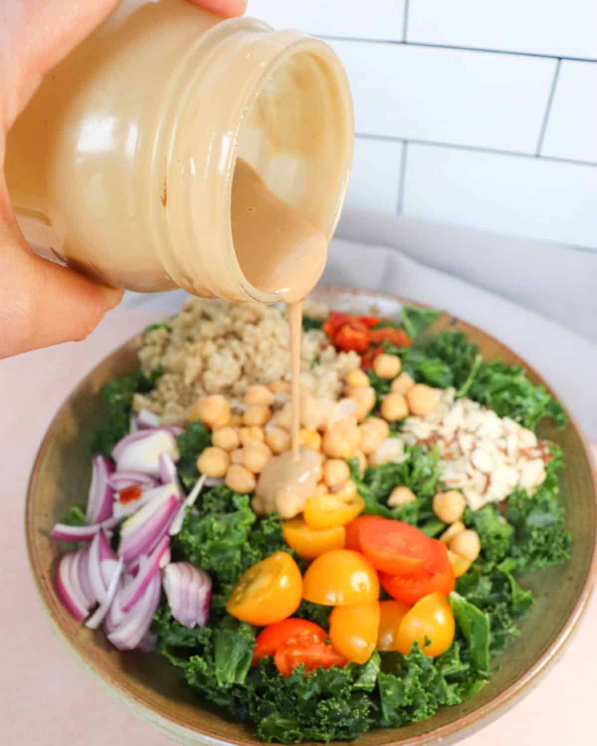 Tahini dressing getting poured over a kale salad.