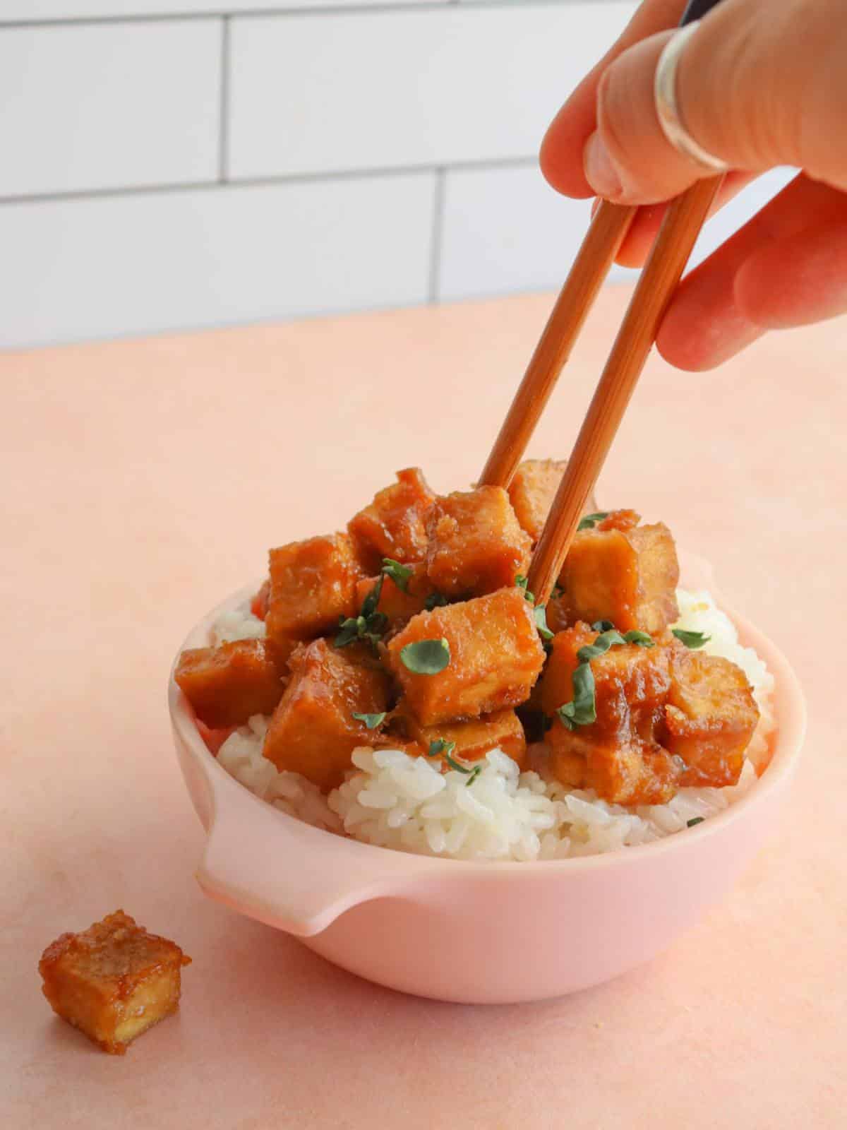 Miso tofu in a bowl with rice and a hand holding chopsticks.