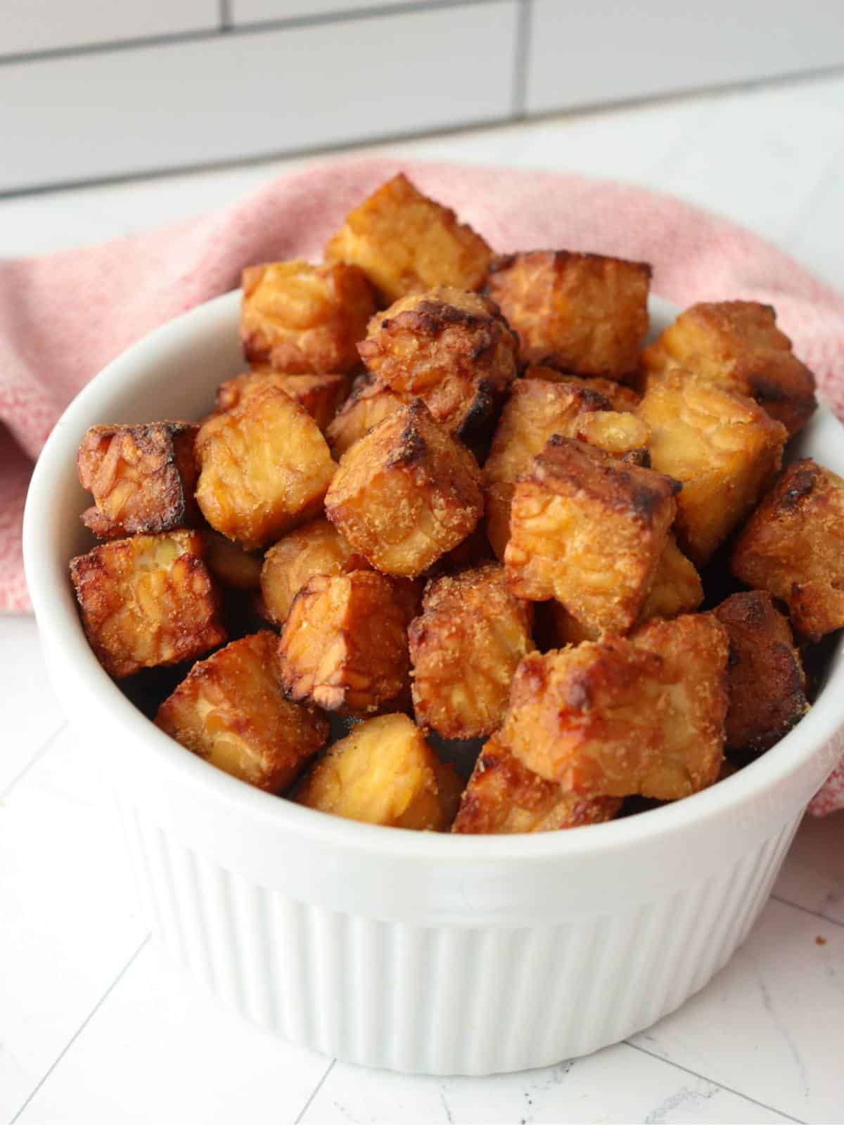Marinated and air fried tempeh cubes in a white ceramic bowl.