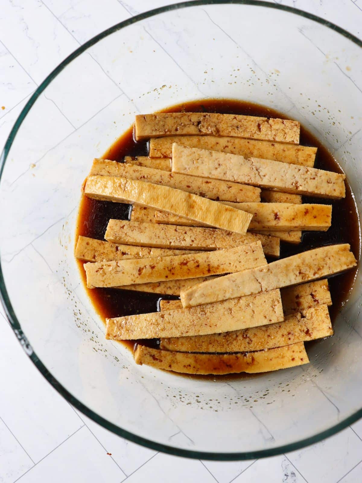 Tofu strips marinating in a soy sauce based marinade.
