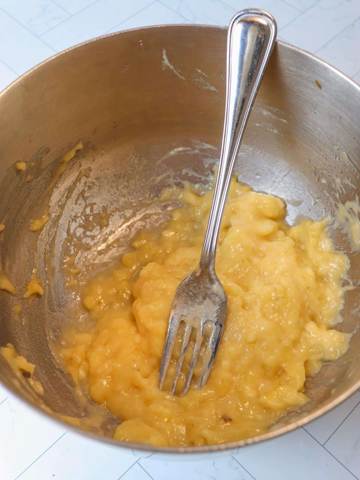 Mashed banana in a mixing bowl with a fork.