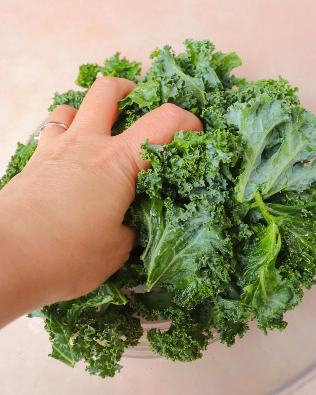 Hand massaging olive oil into kale leaves in a bowl.