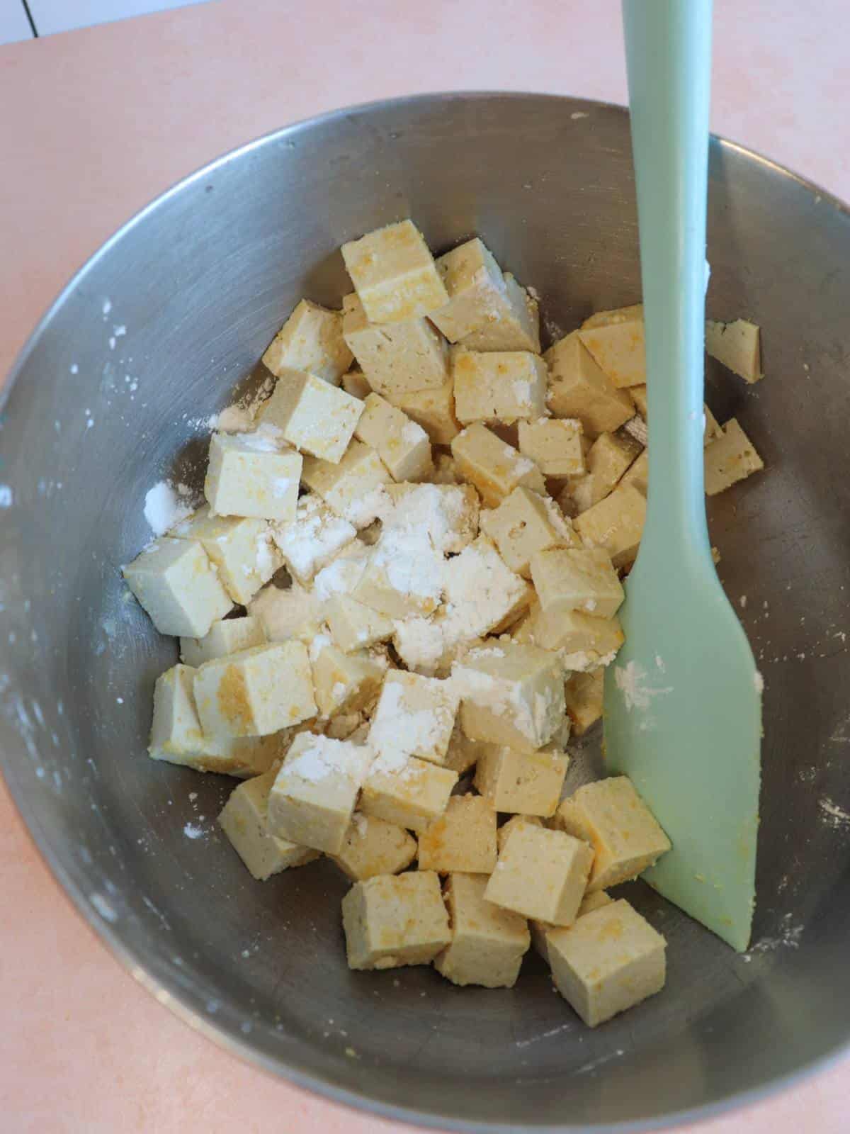 Tofu cubes in a mixing bowl with seasonings and corn starch.