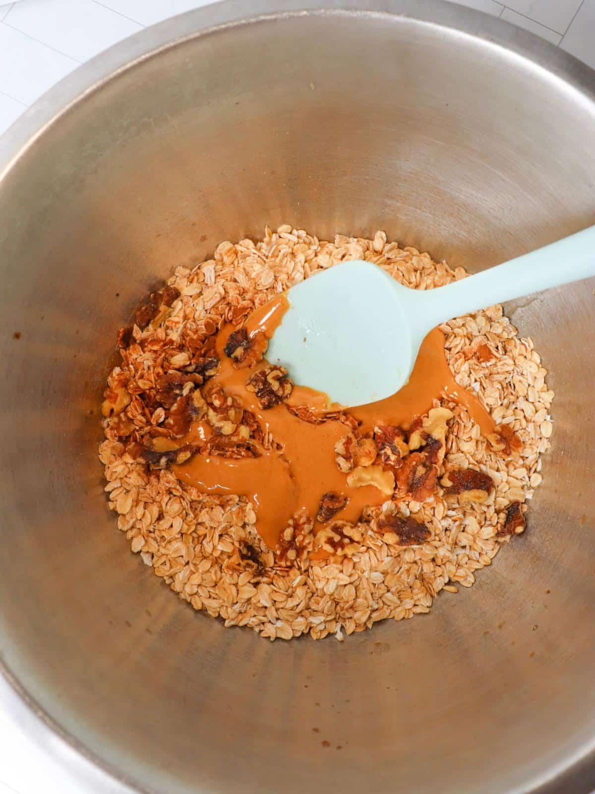 Vegan granola ingredients in a mixing bowl with a rubber spatula.