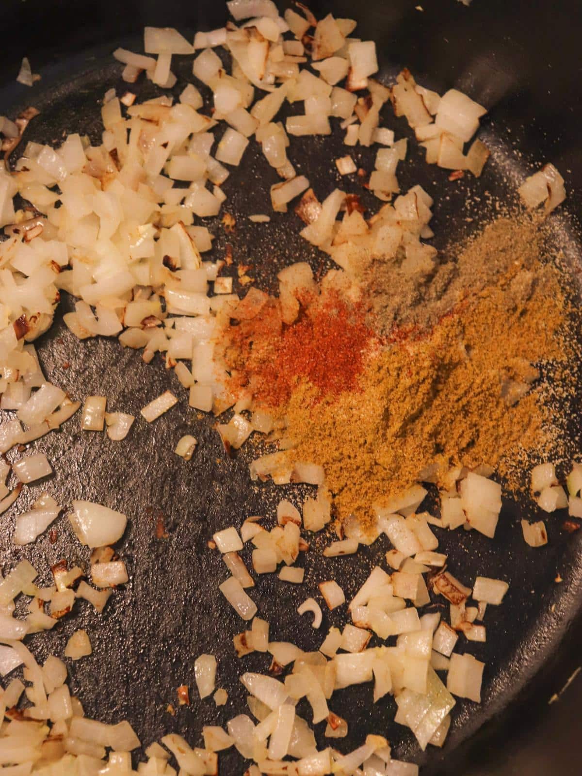 Onions and spices in a sauté pan on a stove.