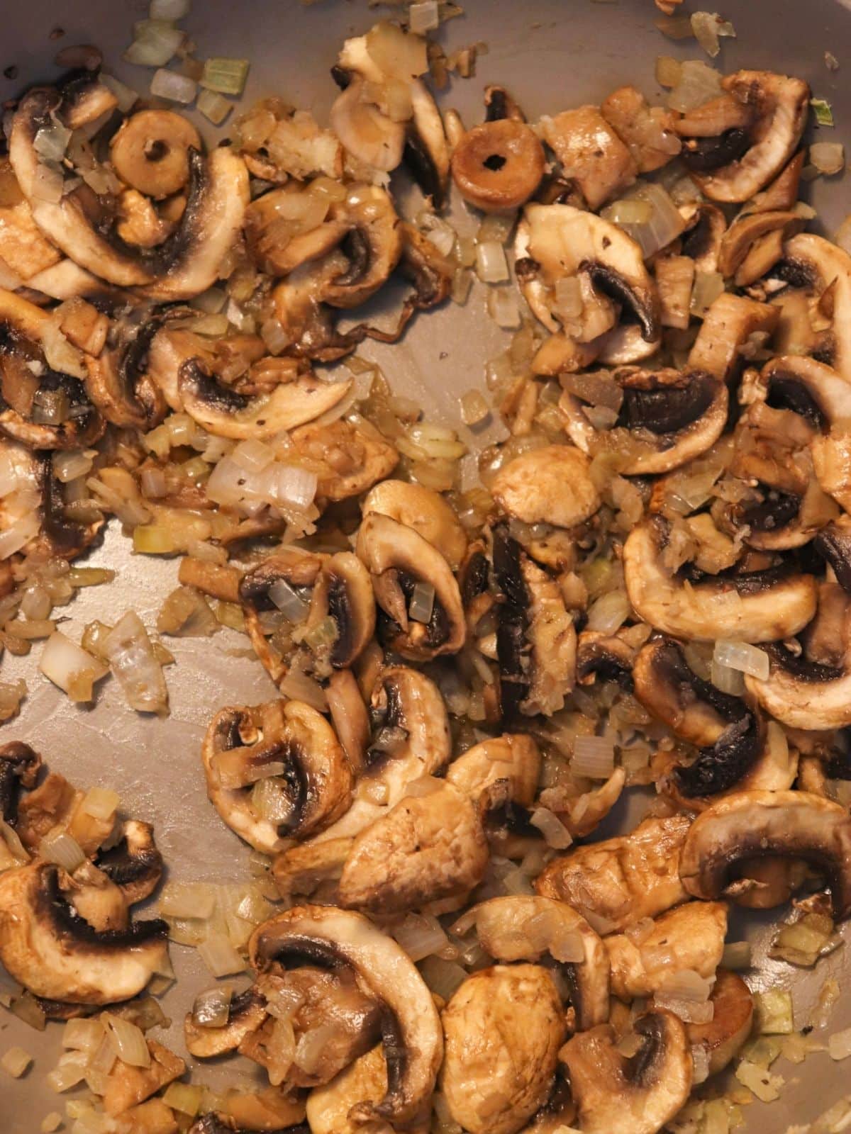 Mushrooms and onions sautéing in a frying pan.