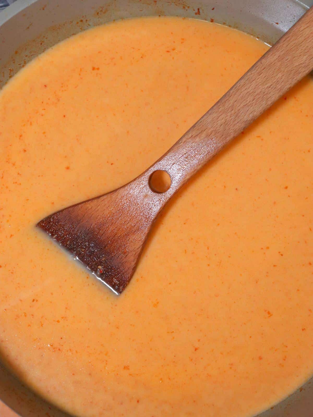 Vegan red thai curry sauce with coconut milk in a pan with a wooden spoon.