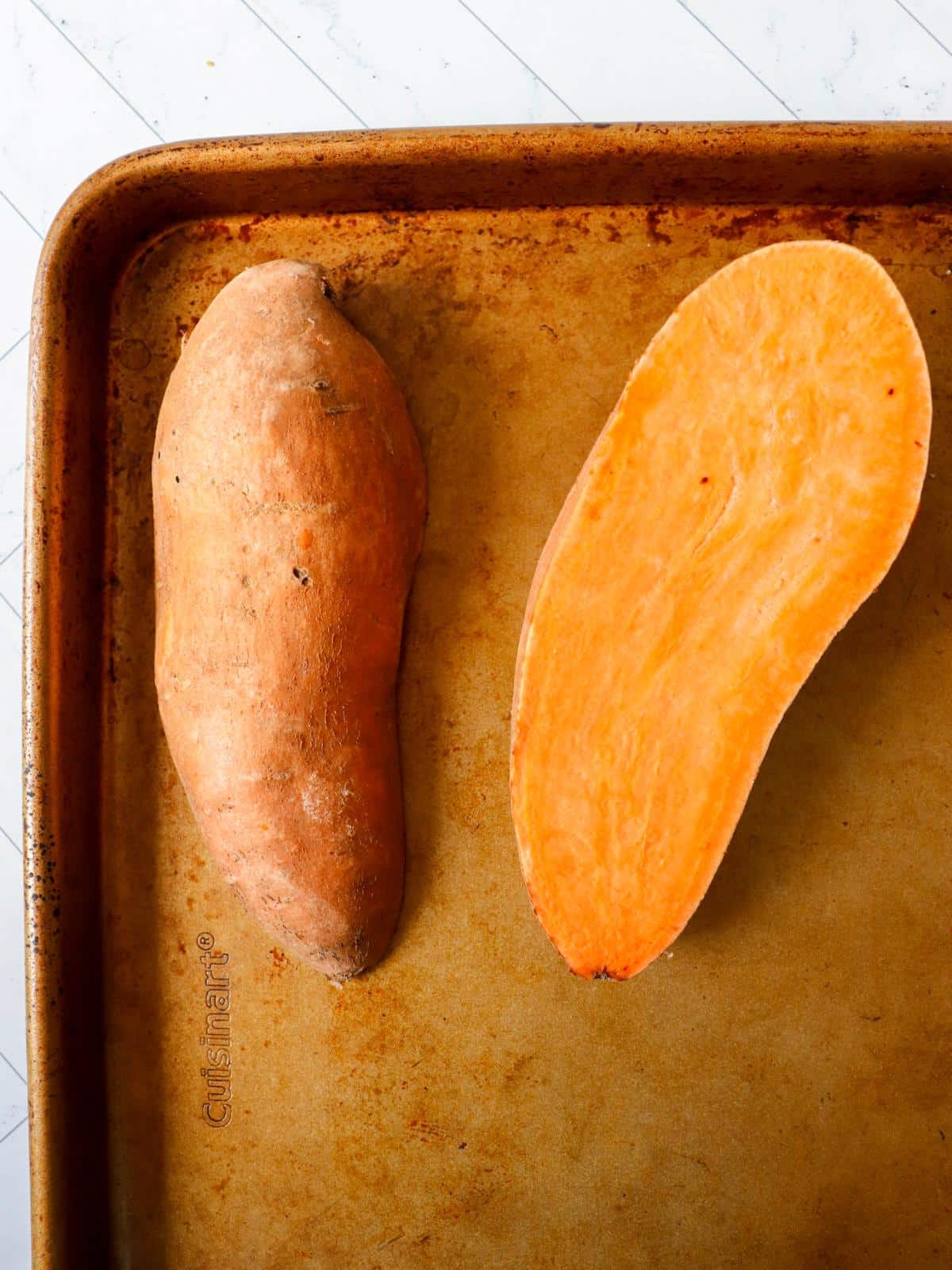 A sweet potato cut in half on a baking sheet.
