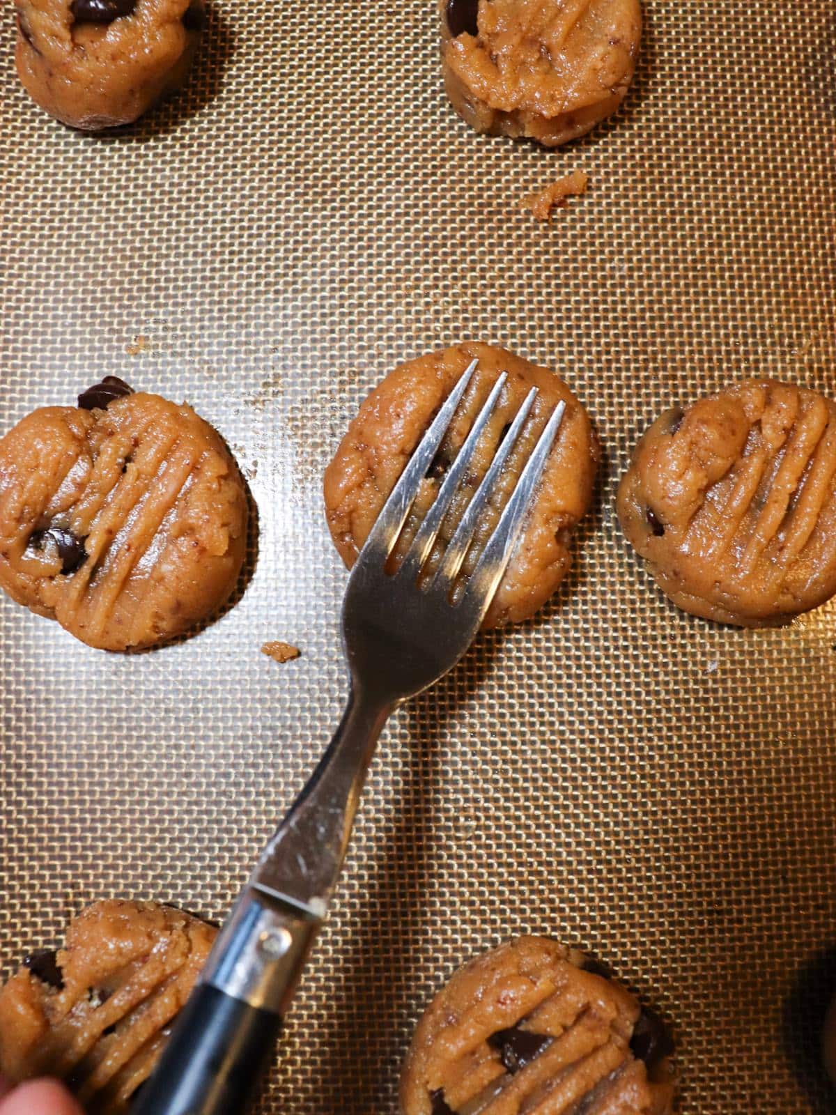 Vegan peanut butter cookie dough balls on a baking sheet getting pressed down and shaped with a fork.