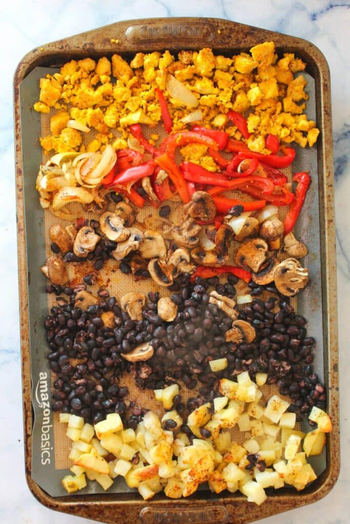 A row of tofu scramble, bell peppers and onions, mushrooms, black beans and hashbrowns on a baking sheet pan.