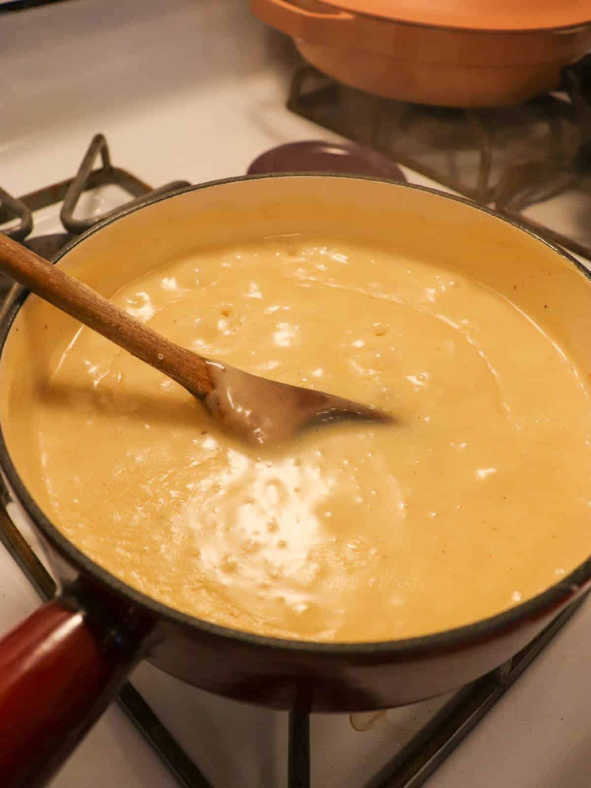 Melted vegan cheese in a fondue pot with a wooden spoon.