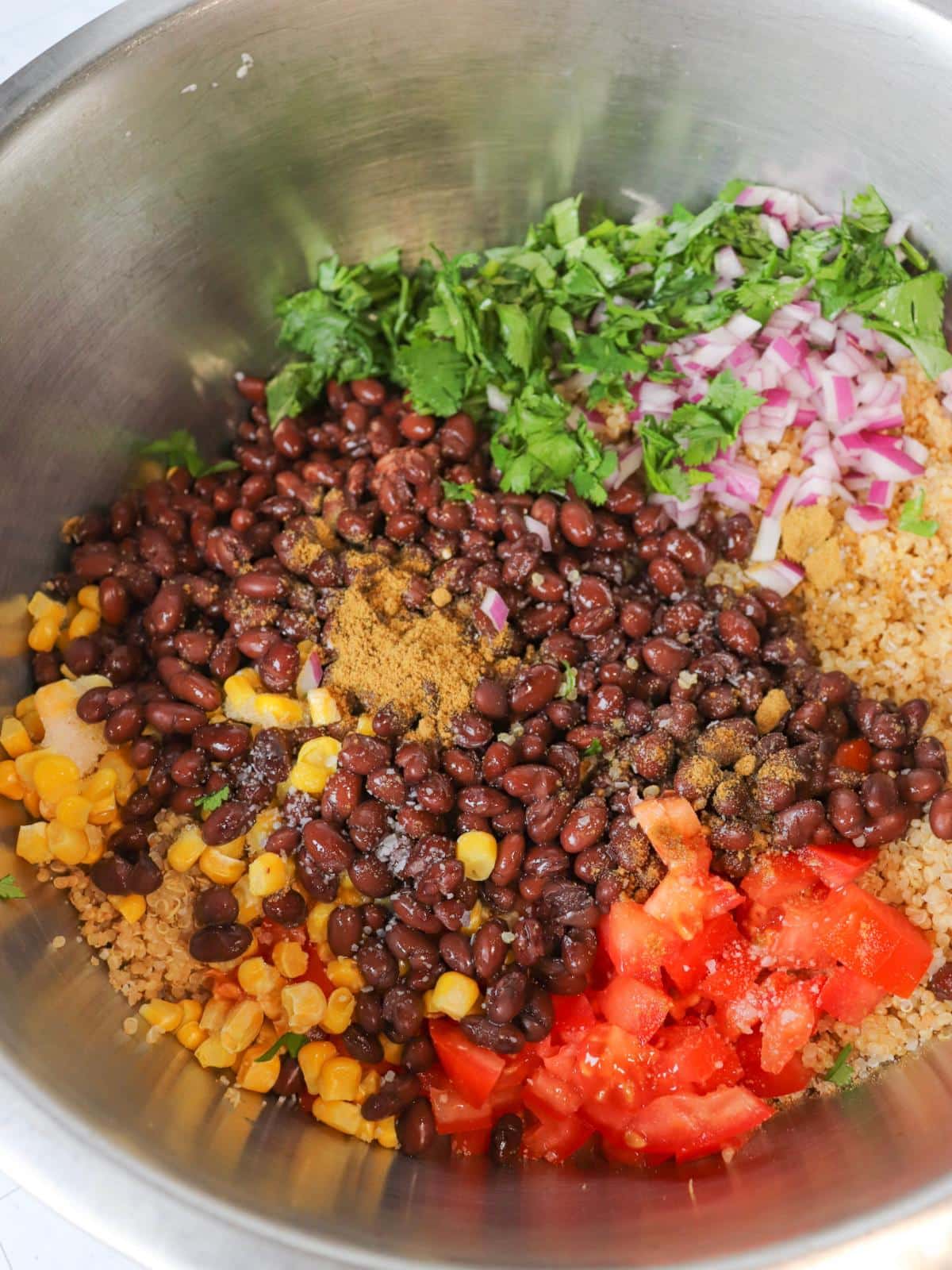 All the ingredients for quinoa black bean salad in a large metal mixing bowl before getting mixed.
