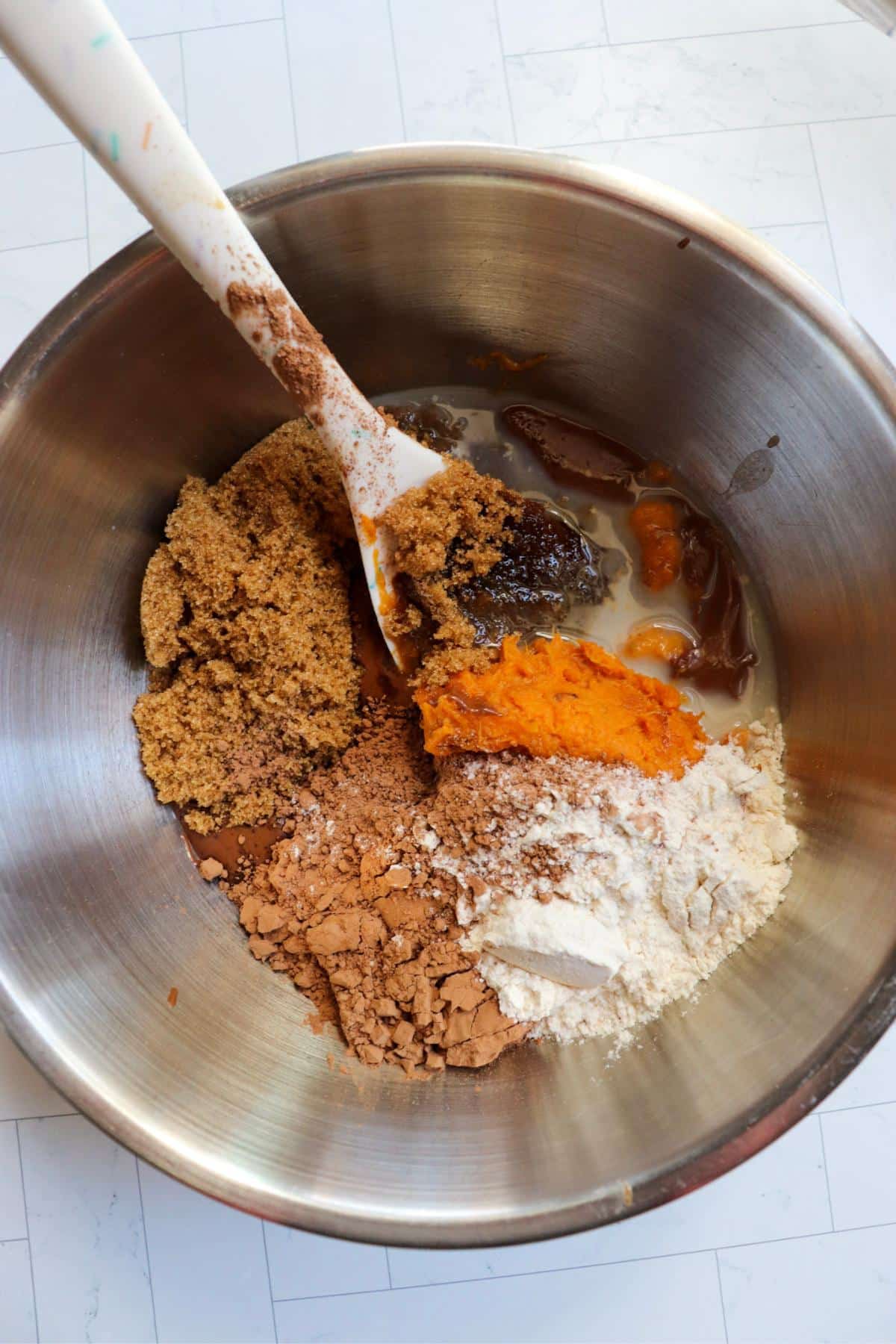 Unmixed sweet potato brownie ingredients in a mixing bowl with a rubber spatula.