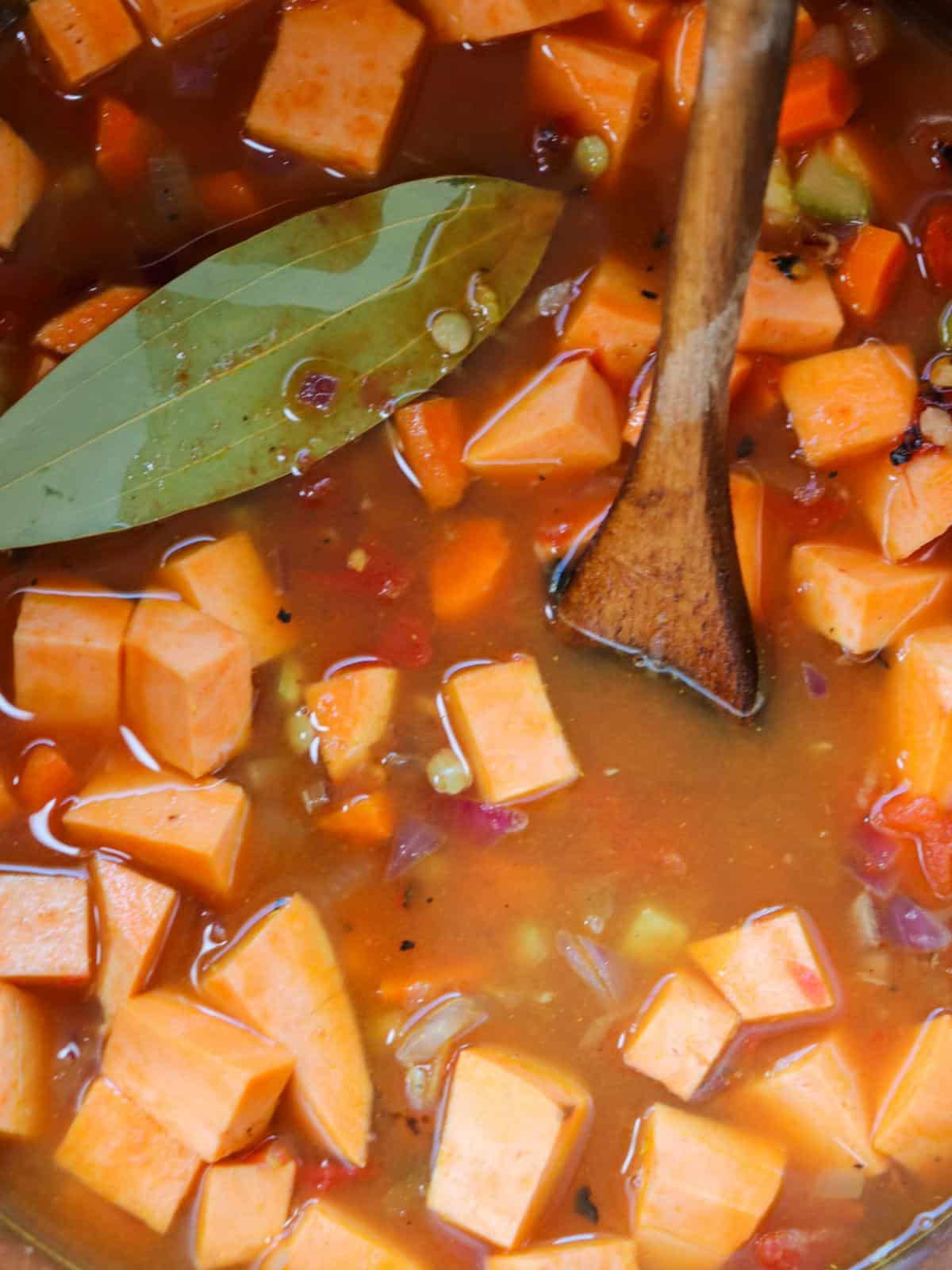 Sweet potato and lentil soup in a pot with a bay leaf and wooden spoon.