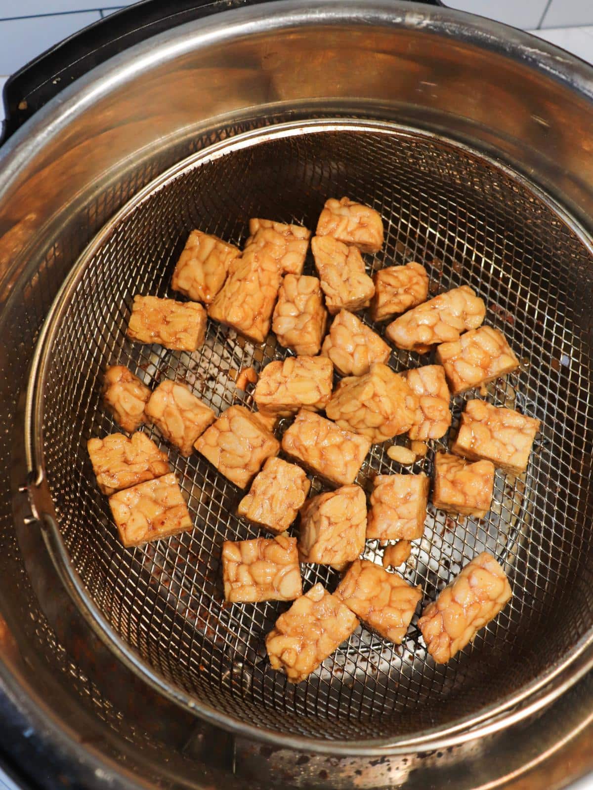Marinated tempeh cubes in an air fryer before getting air fried.