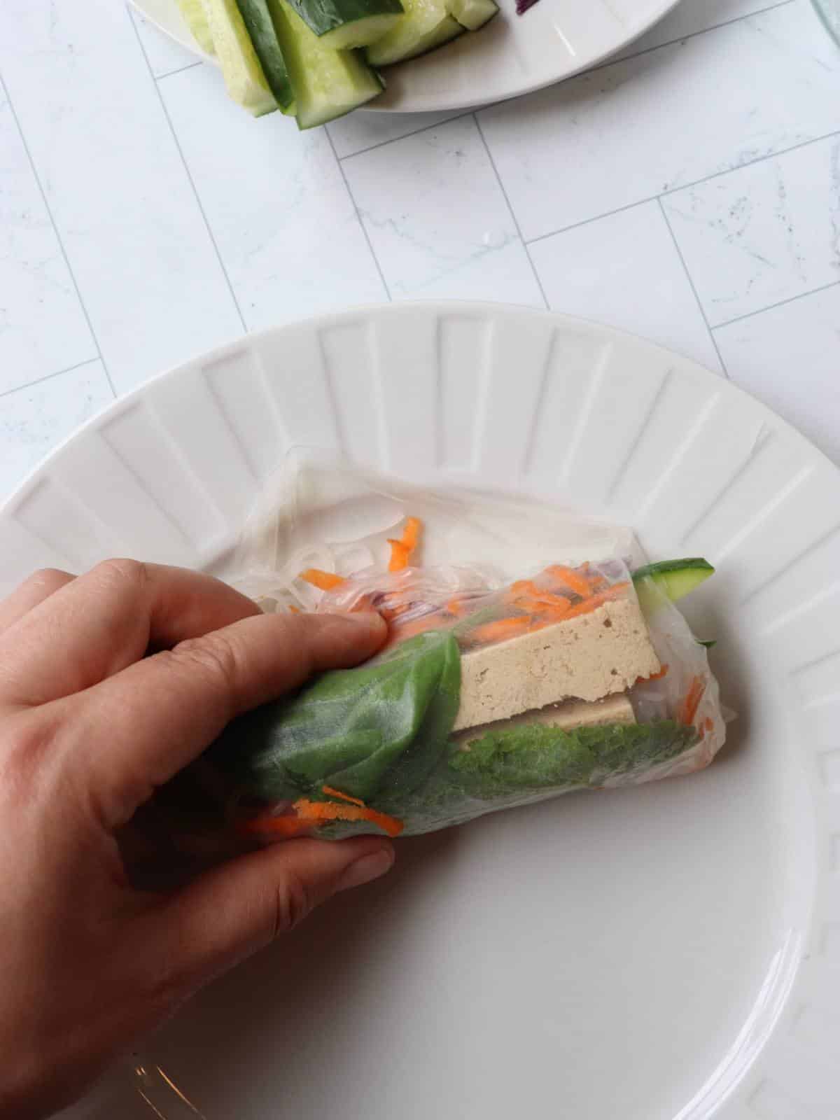 Hand rolling up a vegan Thai tofu fresh roll.
