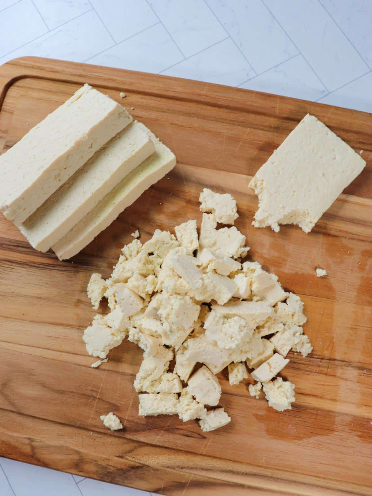 Tofu being cut into slices, then torn into bite sized pieces.