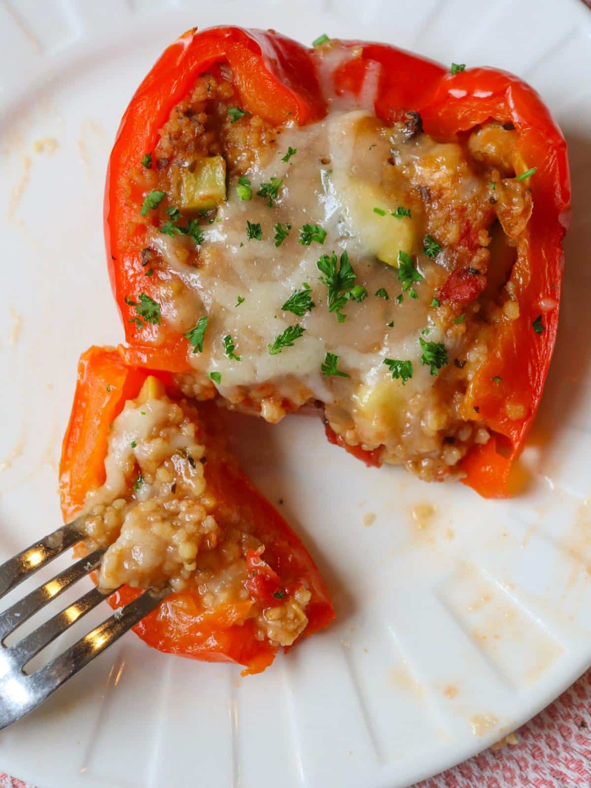 A stuffed couscous bell pepper on a plate with a fork cutting into it.