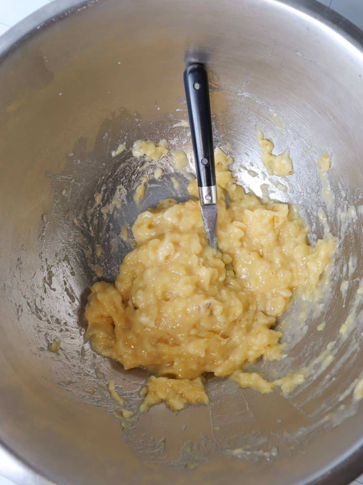 Mashed banana in a mixing bowl with a fork.
