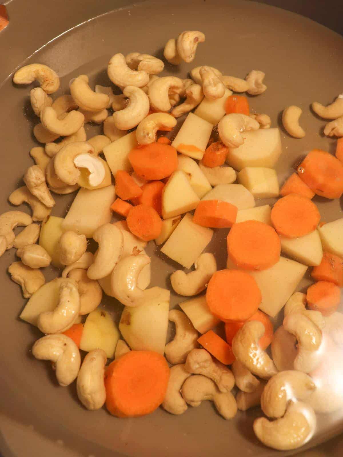 Raw cashews, potatoes and carrots simmering in a pan on the stove.