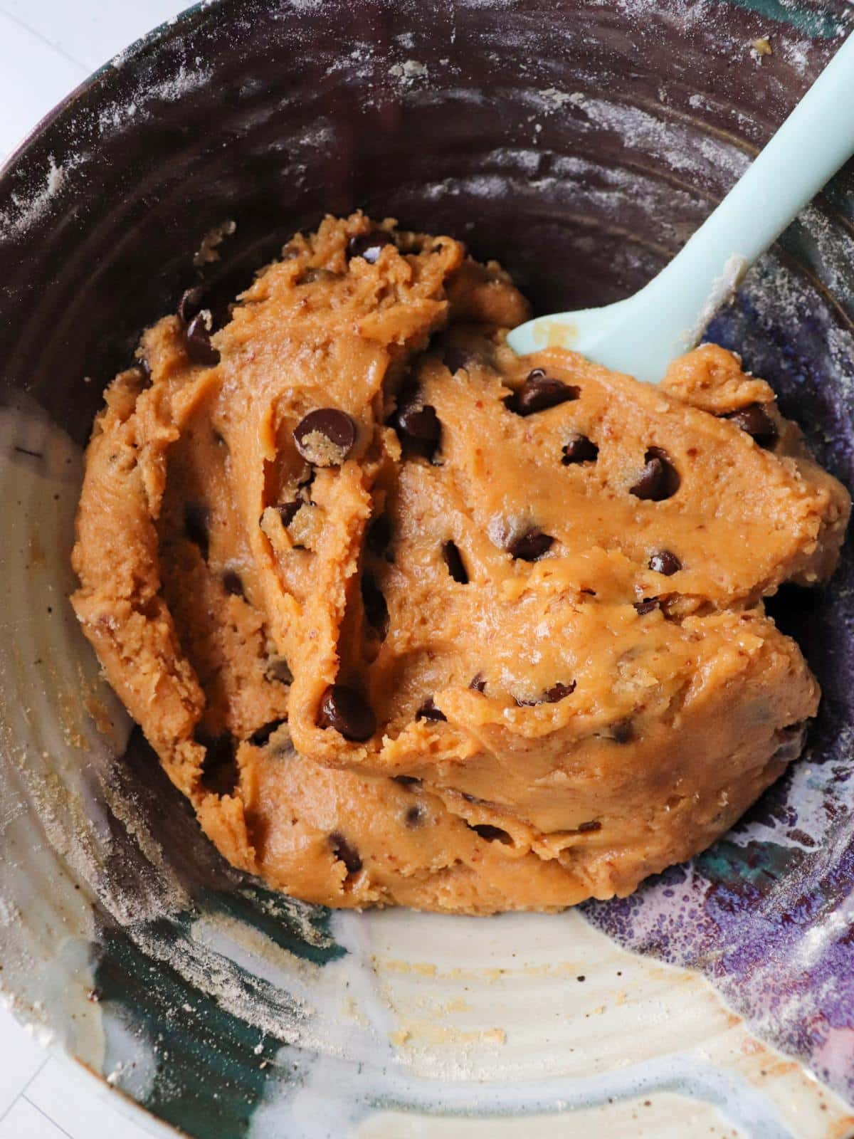 Vegan peanut butter chocolate chip cookie batter in a mixing bowl with a blue spatula.
