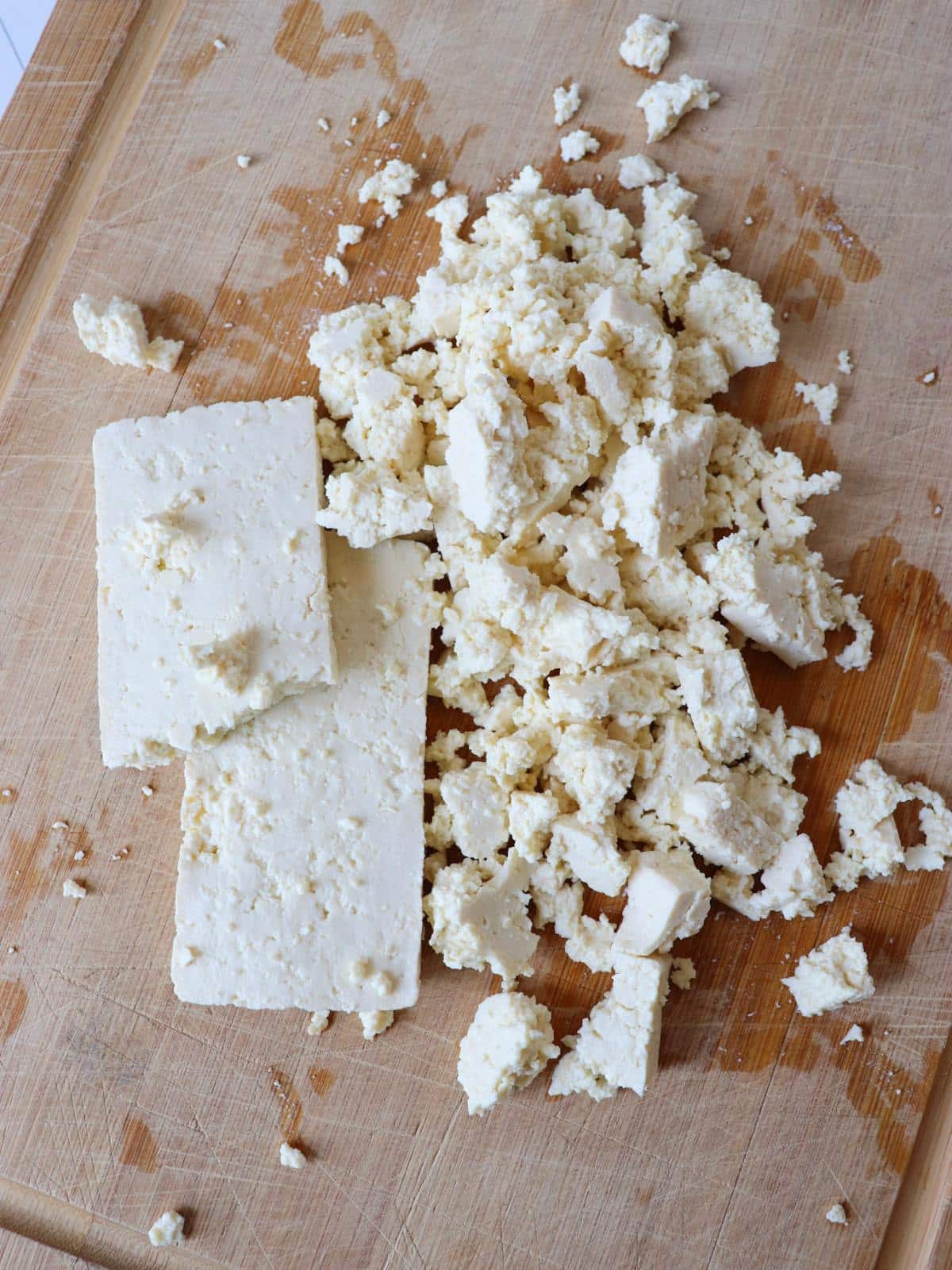 Tofu slices being crumbled on a wooden chopping board.