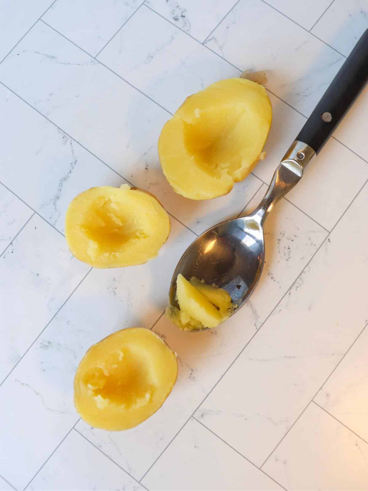 Boiled potato with shallow holes being dug out of the center with a spoon.