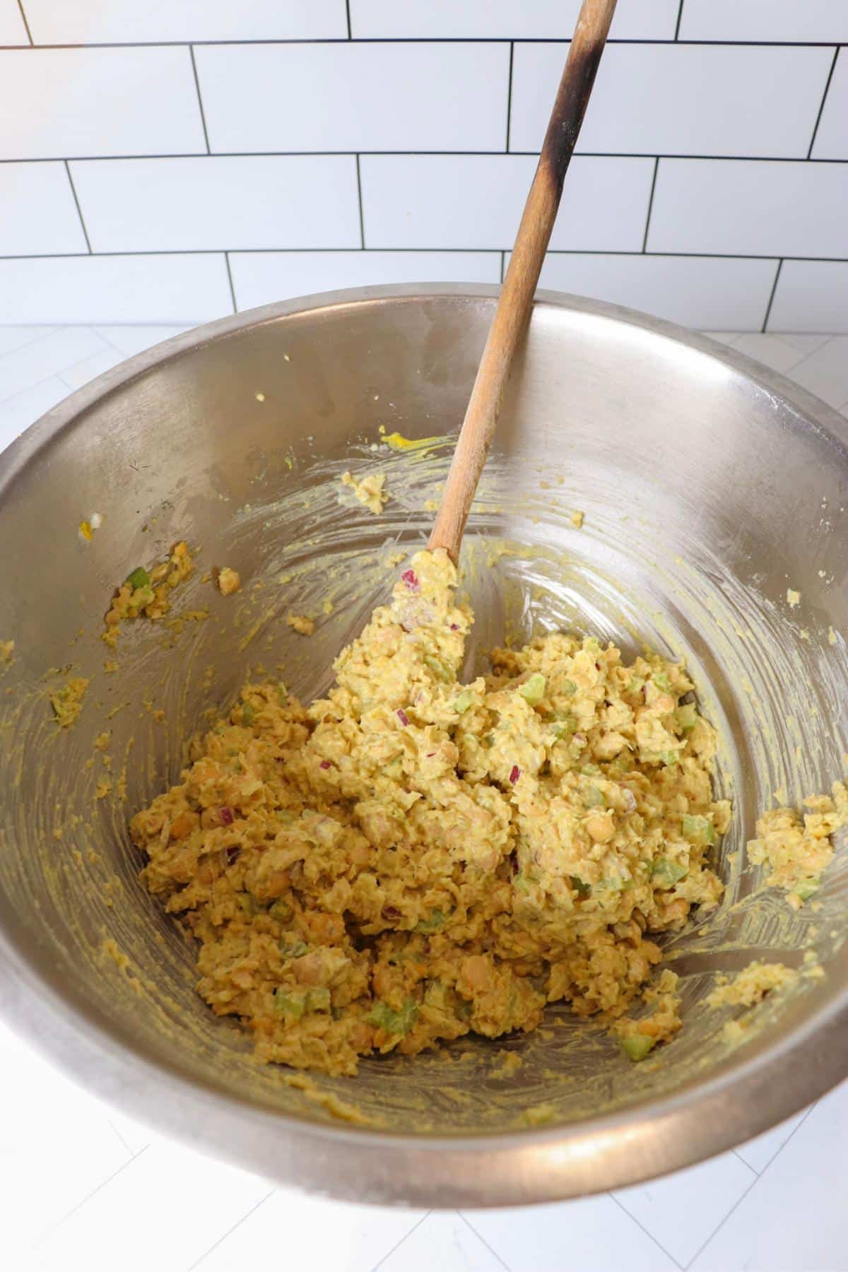 Chickpea salad sandwich ingredients in a mixing bowl after getting mixed together with a wooden spoon.