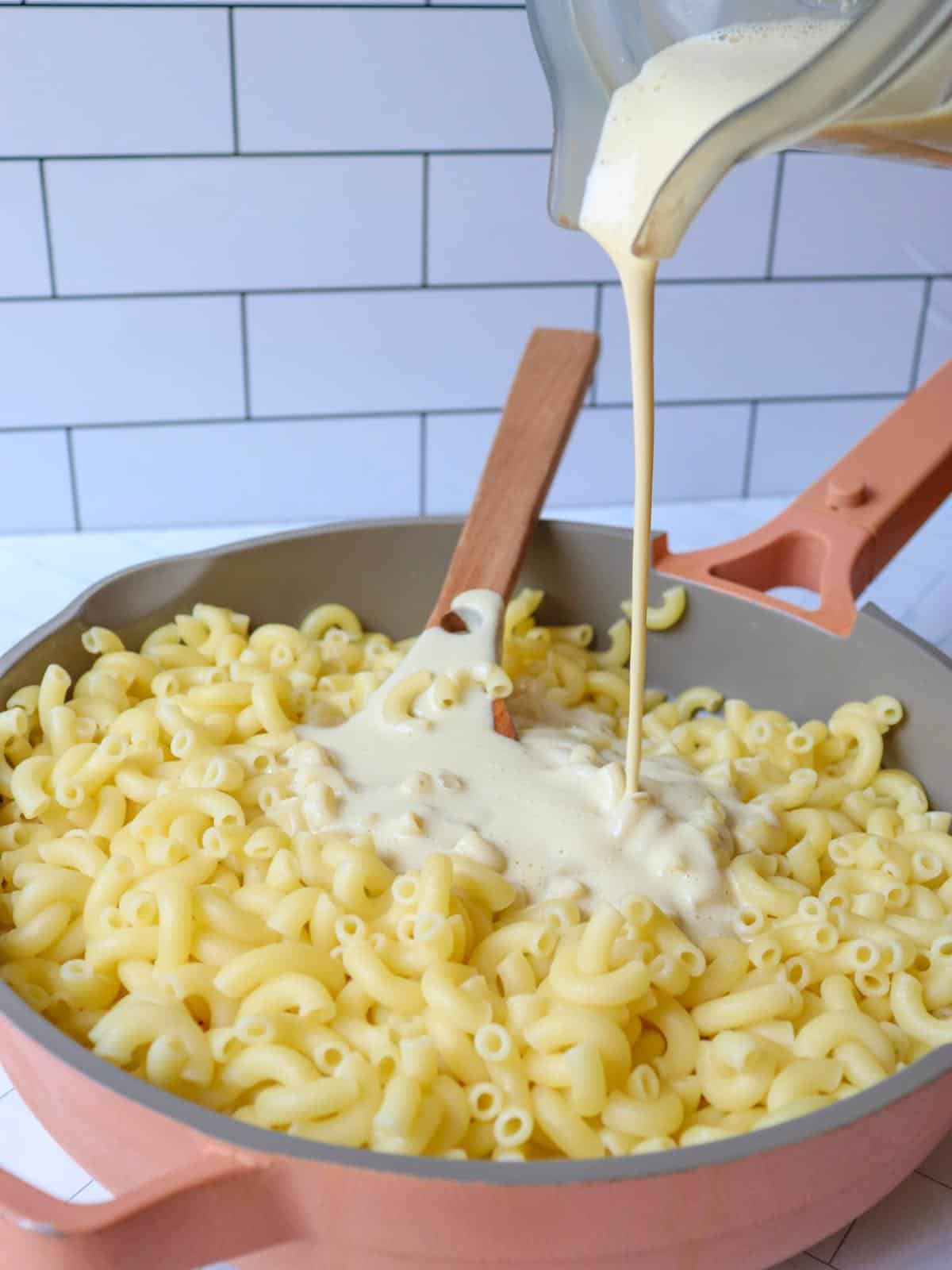 Macaroni noodles in a pan with vegan cheese sauce being poured over them.