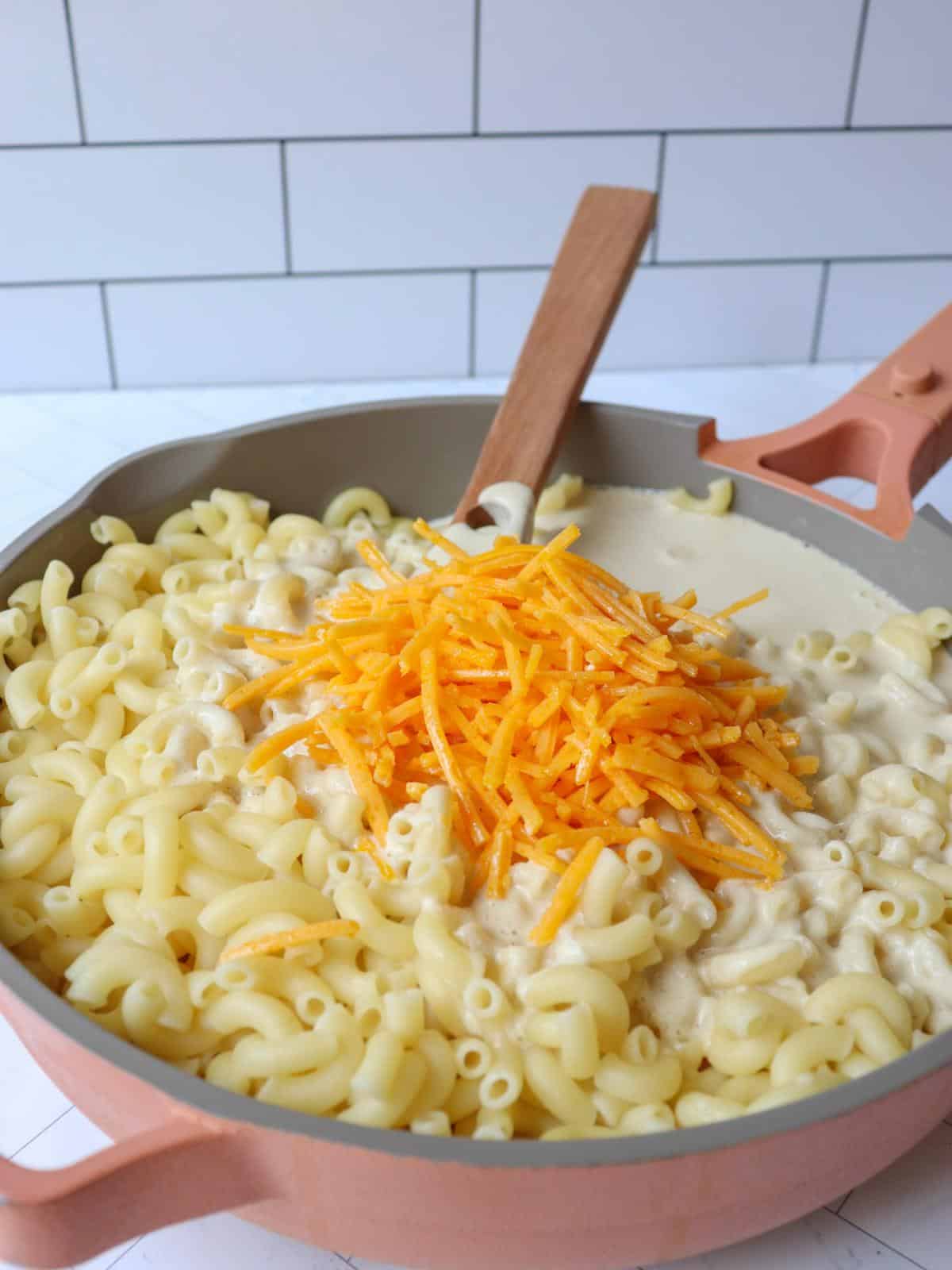 Macaroni noodles in a pan on the stove with vegan cheese on top.