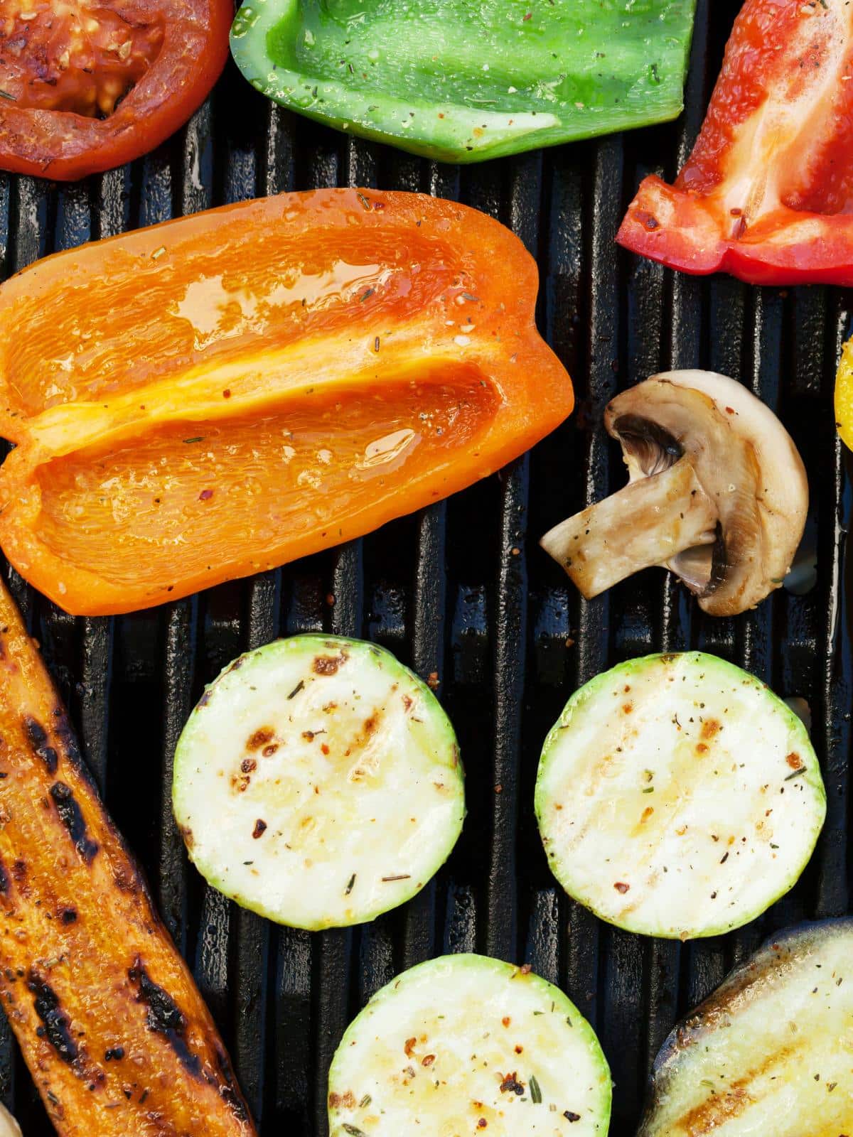 Bell peppers, zucchini and mushrooms grilling on a grill.