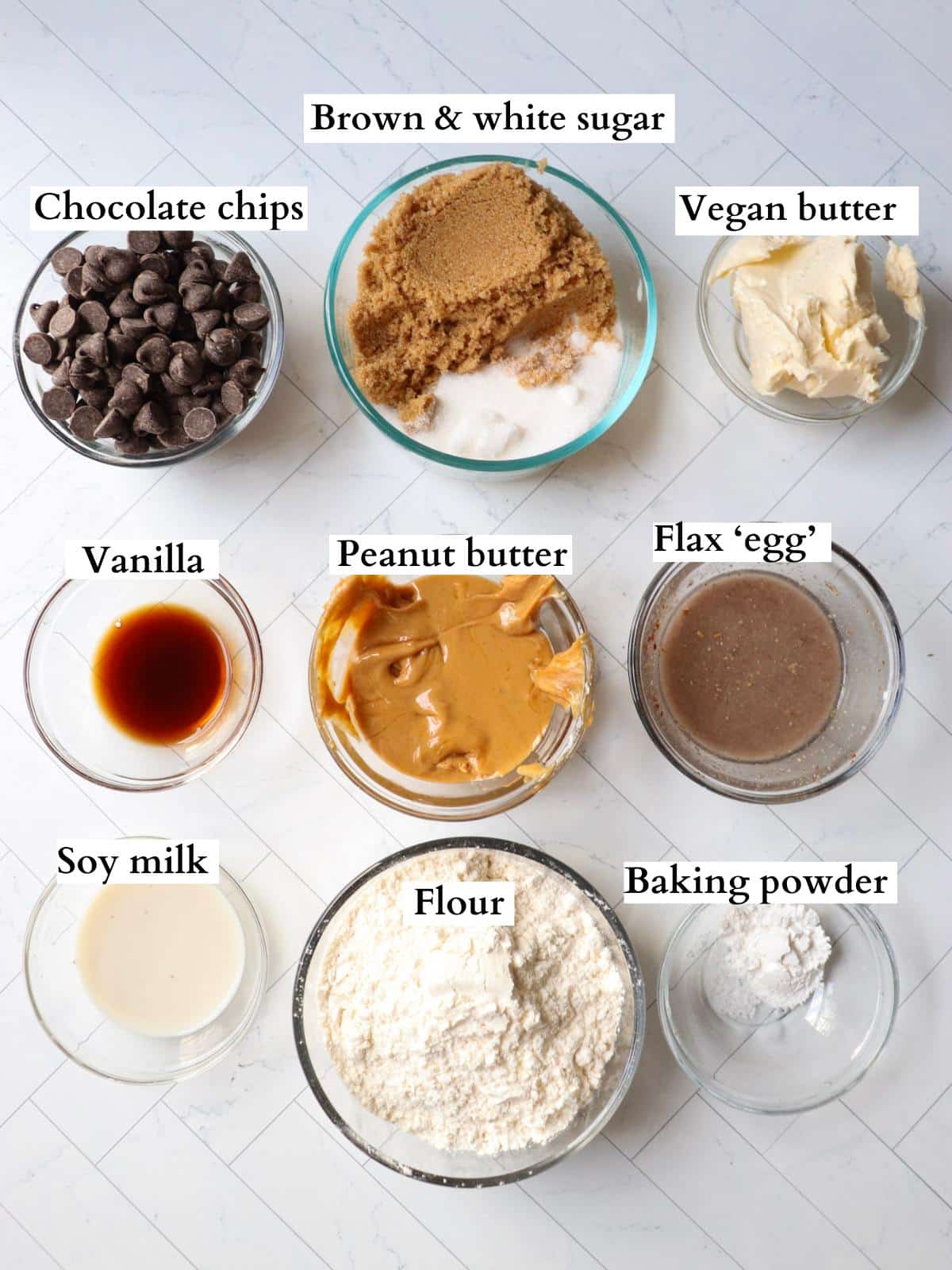 Ingredients for vegan peanut butter chocolate chip cookies laid out in small bowls on a counter.