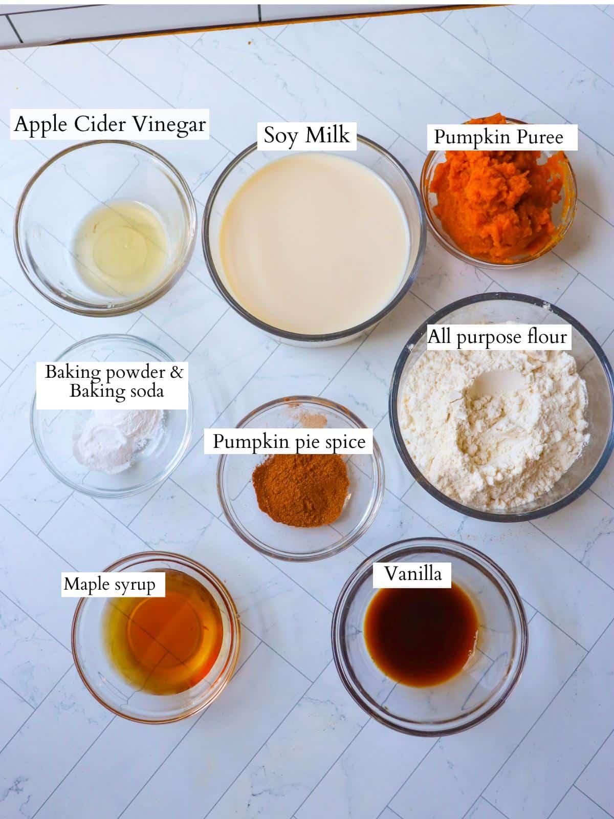 Vegan pumpkin pancake ingredients laid out on a kitchen counter in individual small glass bowls.
