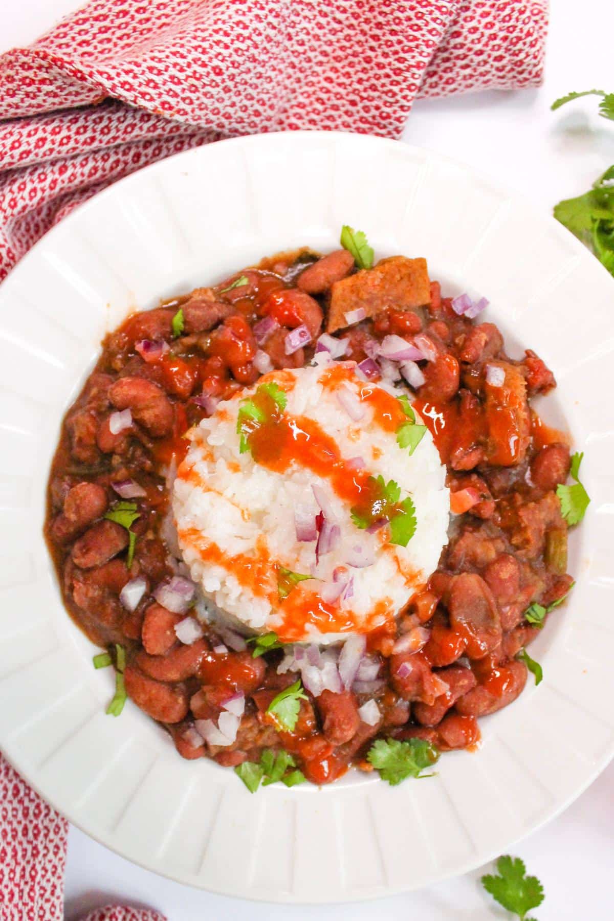 Overhead view of vegan red beans with white rice and topped with hot sauce and fresh cilantro. 