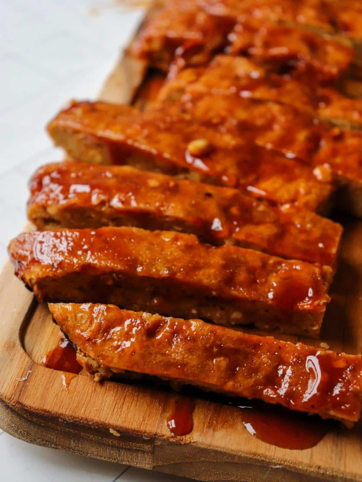 Vegan ribs laid out on a wooden cutting board topped with bbq sauce.